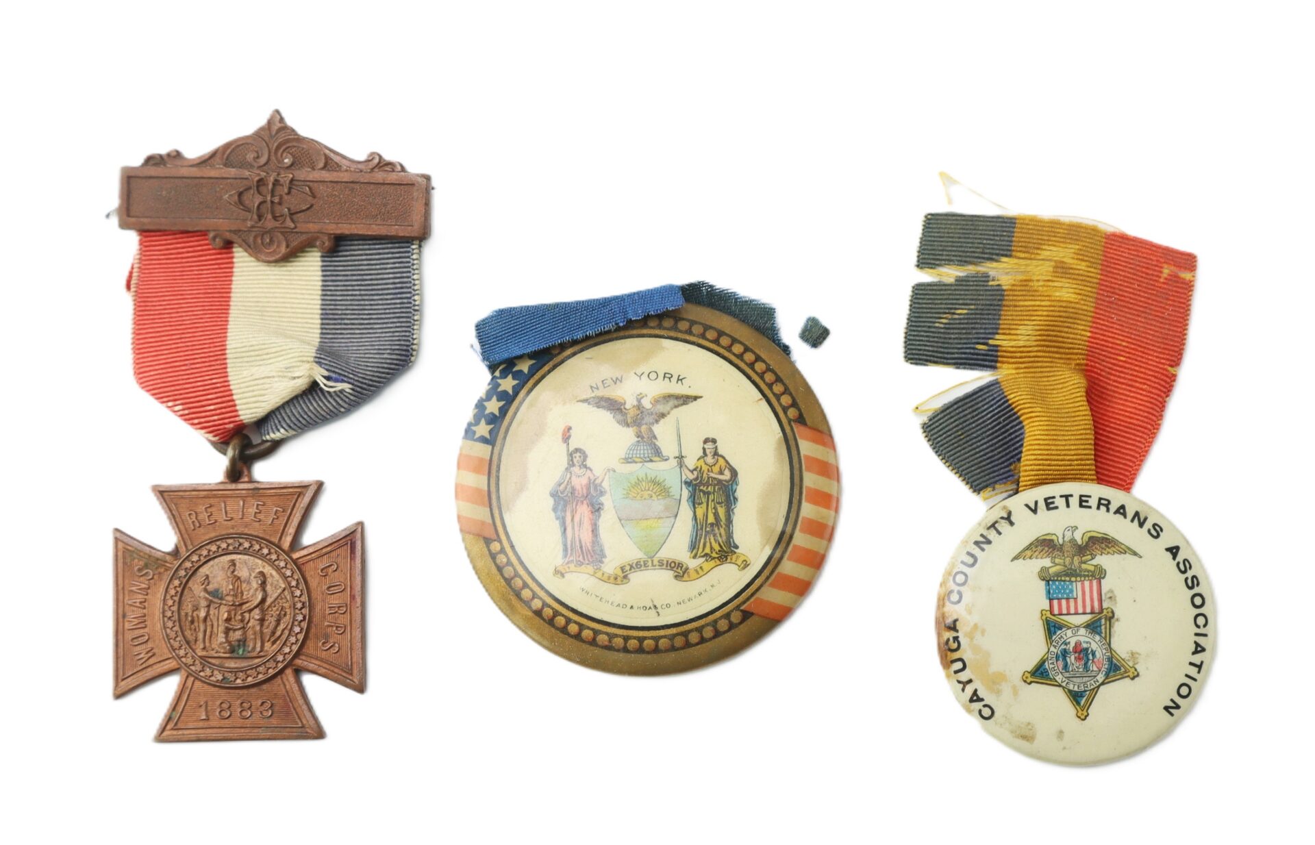 Three vintage badges: a bronze medal with a striped ribbon, a circular New York seal pin with a blue ribbon, and a Cayuga County Veterans Association pin with a multicolored ribbon.