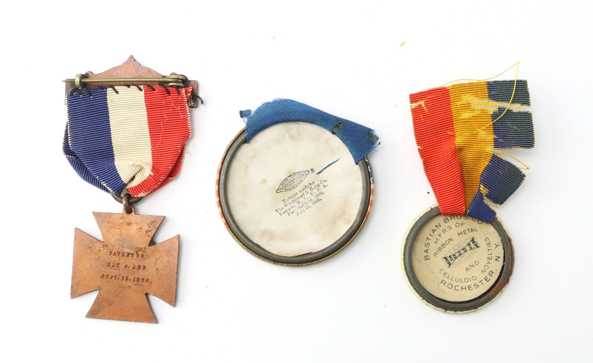 Three vintage medals with colored ribbons, two showing their backs and one showing its front with engraved text, displayed on a white background.