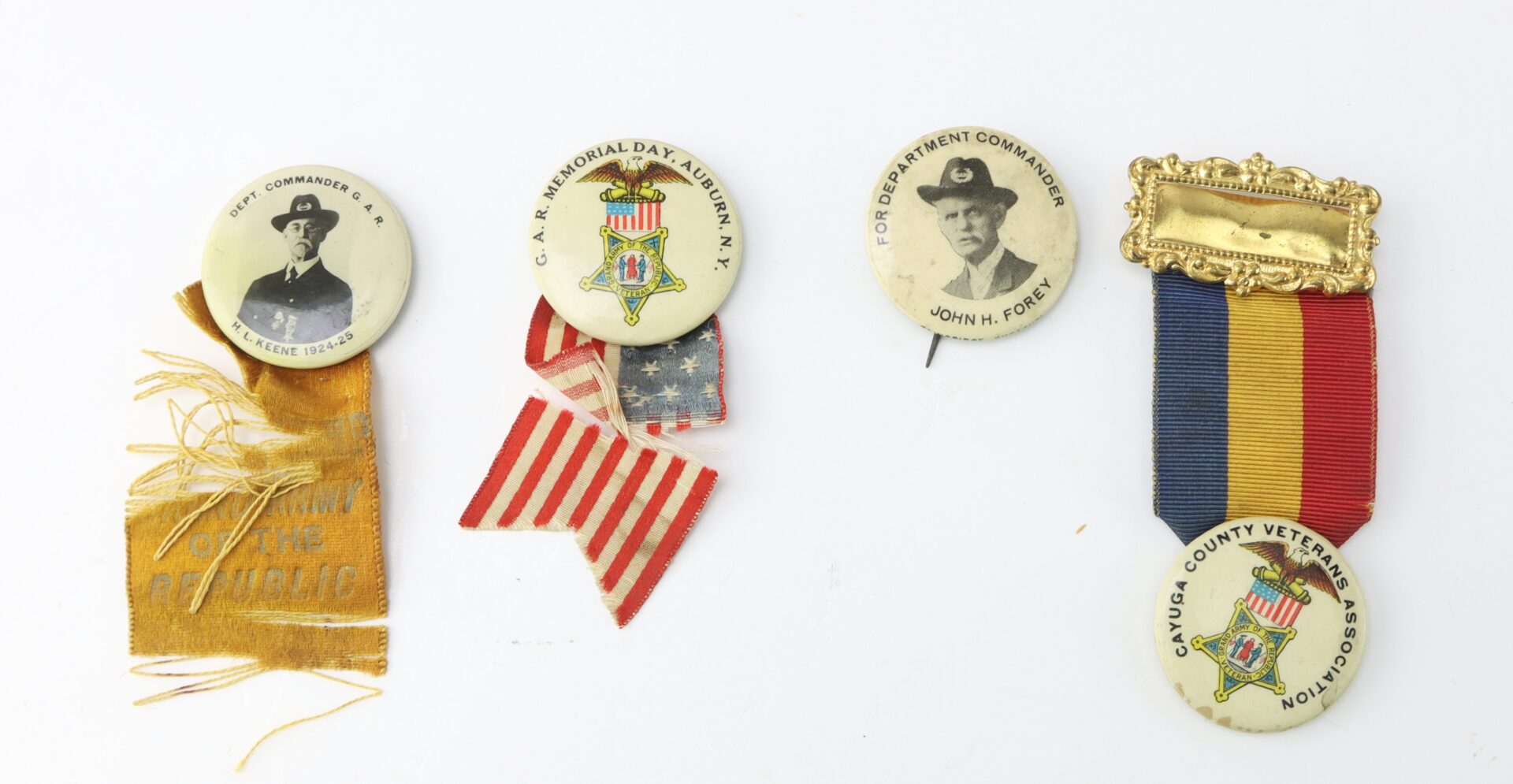 Four vintage military commemorative pins and ribbons, including two pinback buttons with portraits, a tattered gold ribbon, a small fabric U.S. flag, and a multicolored medal.
