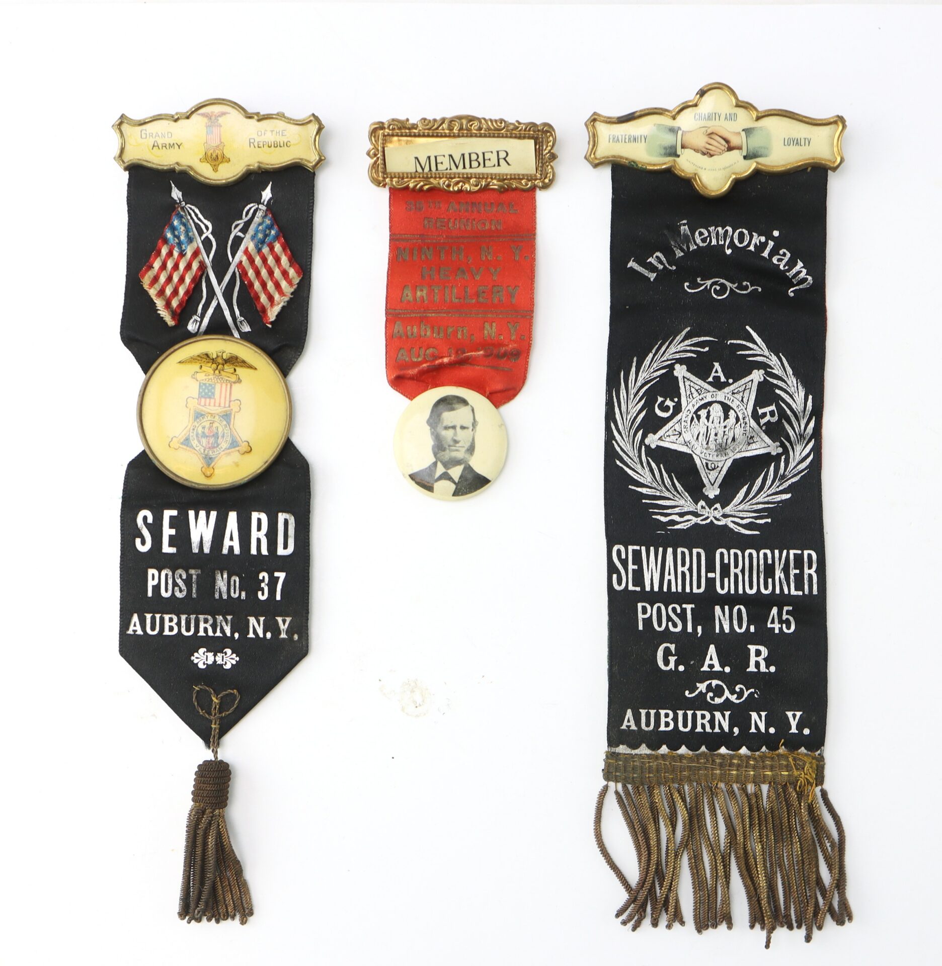 Three vintage Grand Army of the Republic ribbons and a pin, including memorial and membership badges from Auburn, NY, decorated with flags, eagles, and a portrait of Abraham Lincoln.