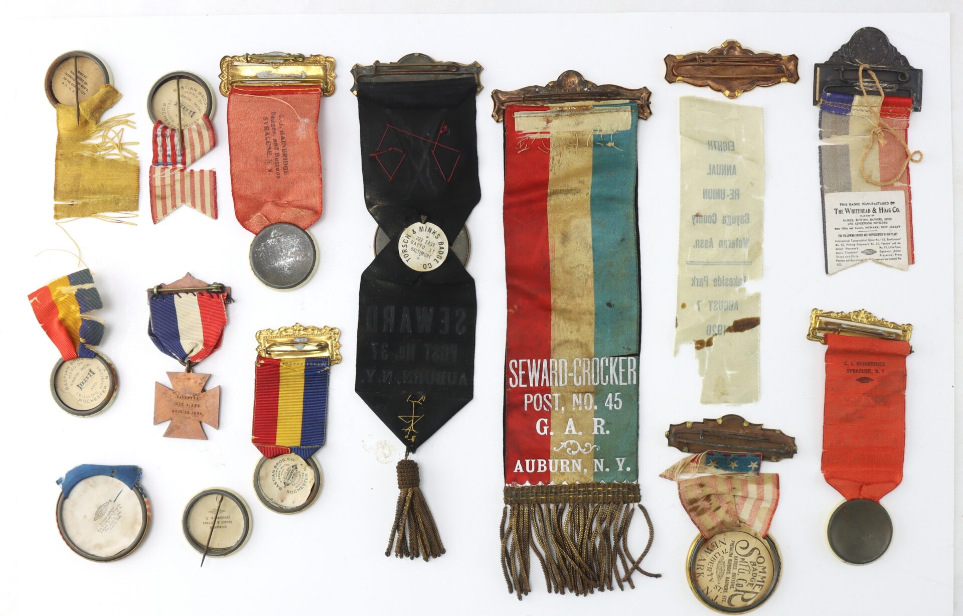 A collection of vintage ribbons, medals, and pins, including a multicolored Seward-Crocker G.A.R. ribbon, arranged on a white background.