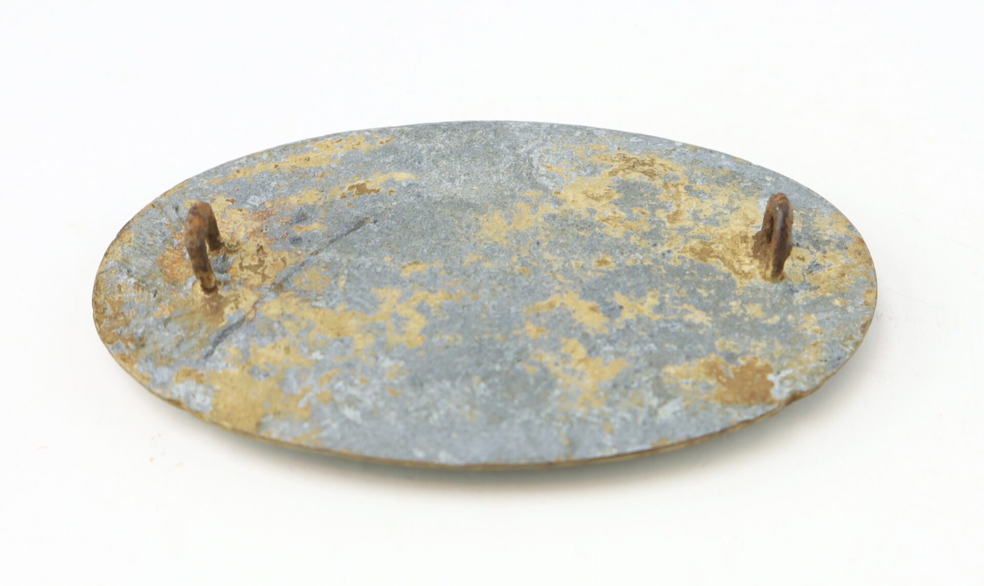 A weathered, oval-shaped metal plate with two rusty hooks attached to one side, displayed on a plain white background.