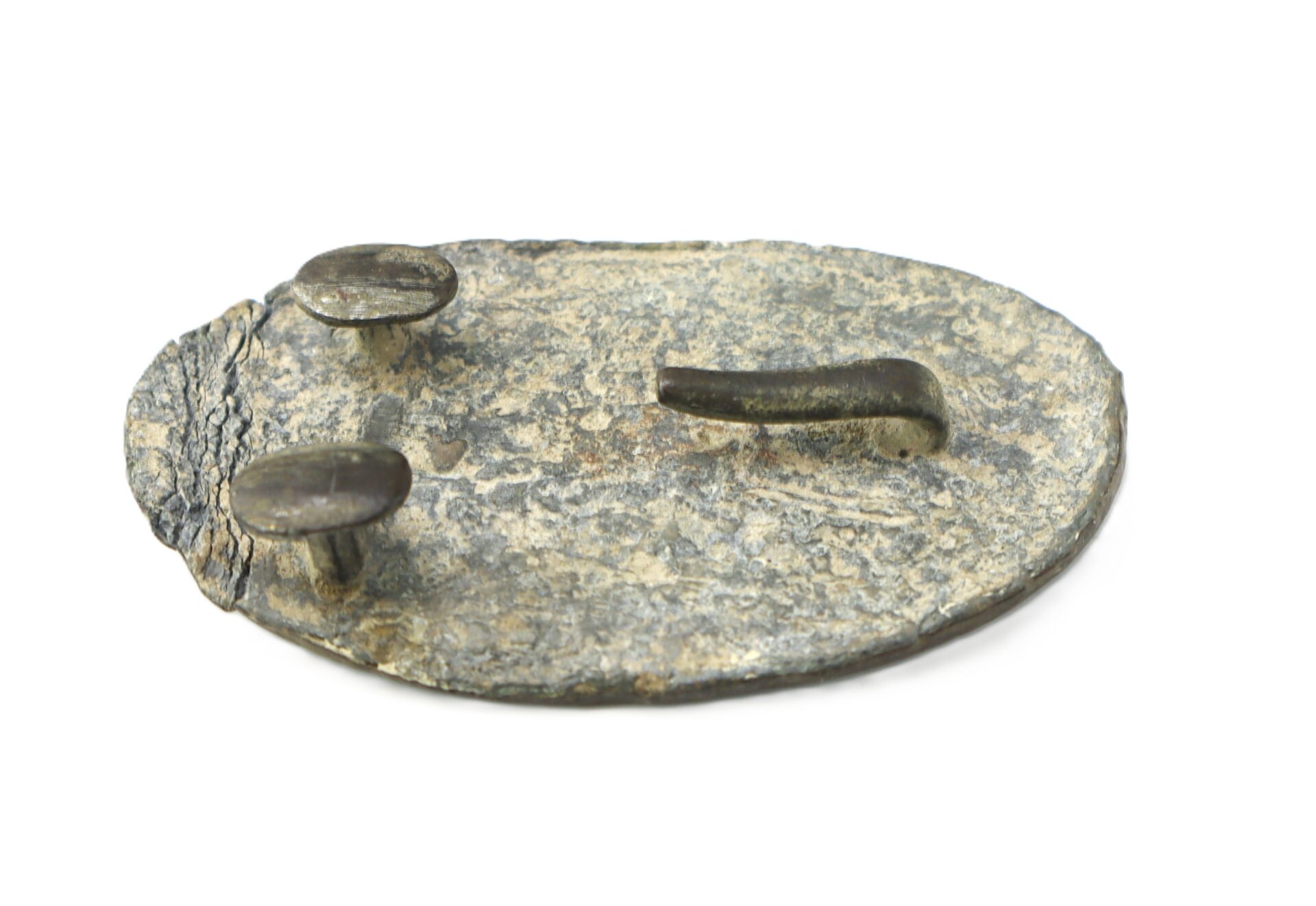 A weathered, oval-shaped piece of metal with two flat-headed pegs and a short curved protrusion on its surface, set against a white background.