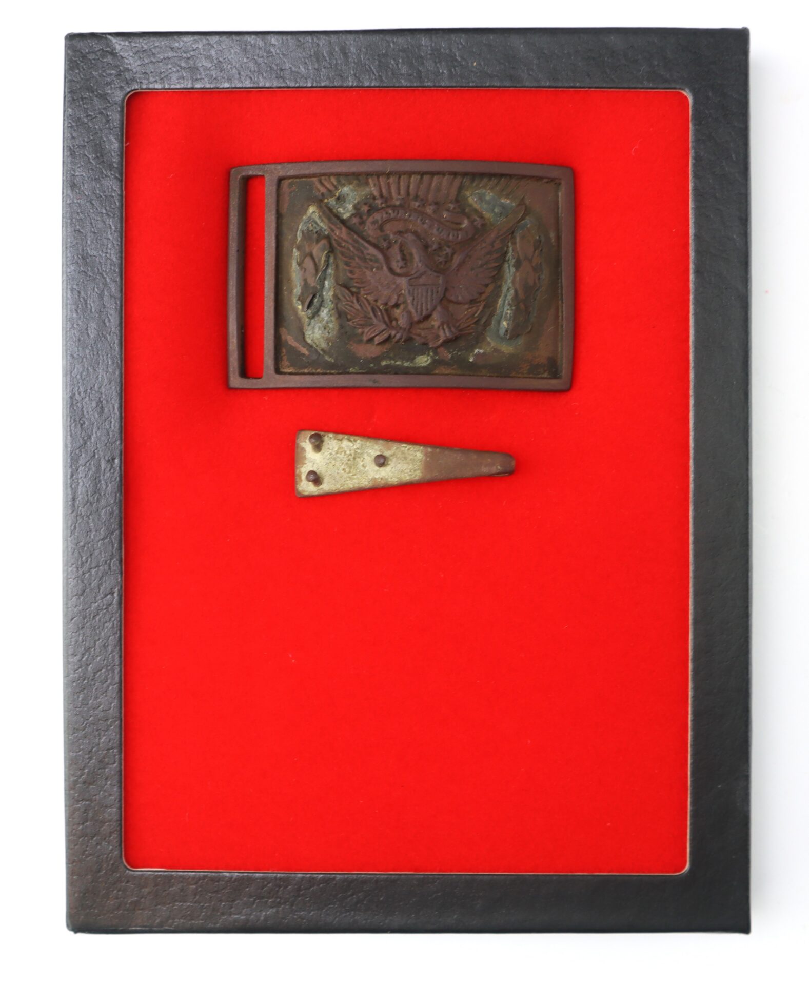 A rectangular black frame displays a bronze belt buckle with an eagle emblem and a separate triangular metal piece on a red background.