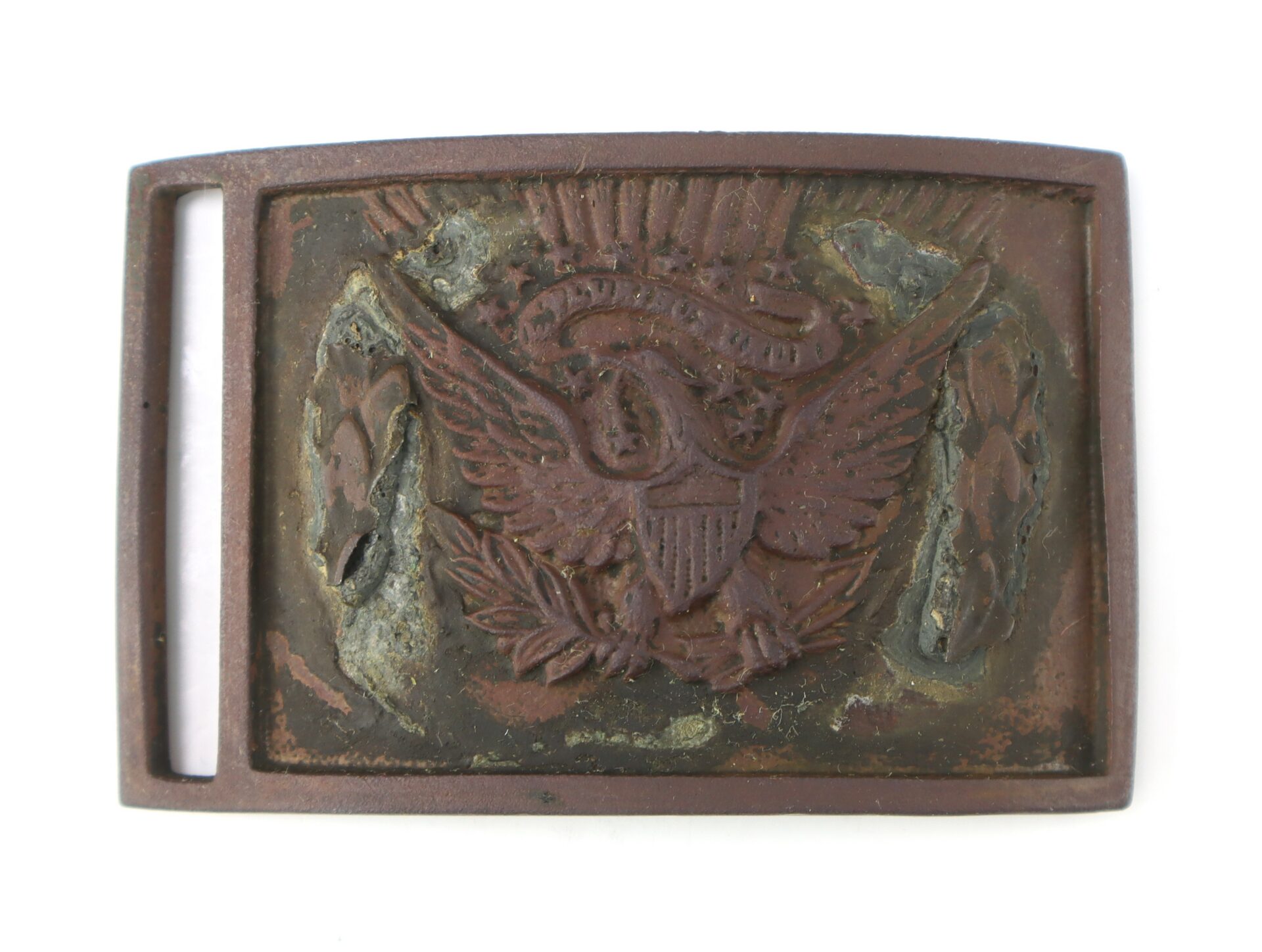 Rusty metal belt buckle featuring an embossed eagle with a shield, arrows, and olive branch, set against a worn background.