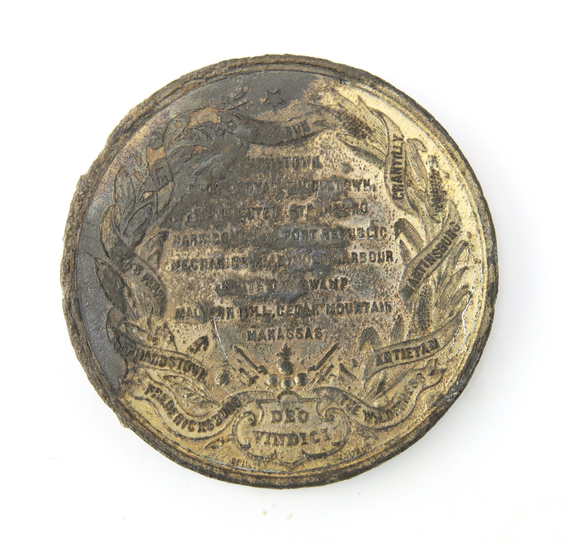 Oval-shaped, tarnished metallic plaque with engraved text, laurel wreath design, and decorative symbols; some inscriptions are difficult to read due to wear.