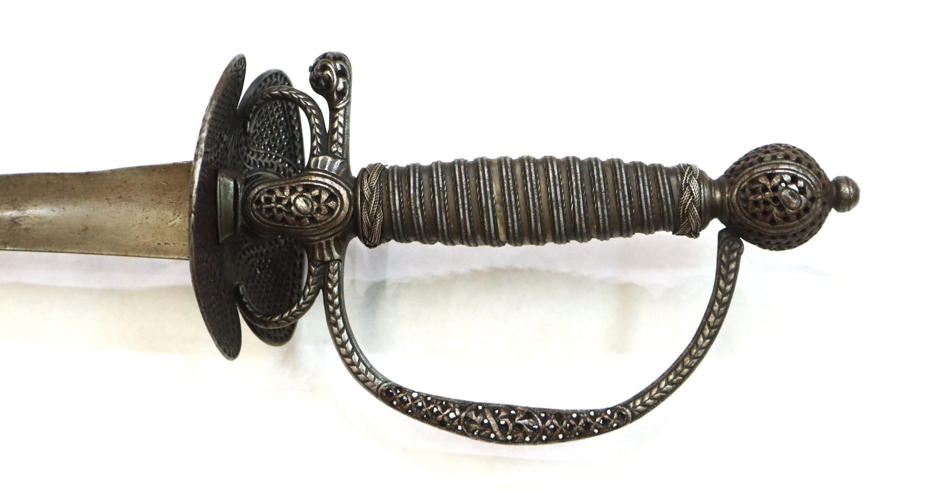 Close-up of an ornate antique sword hilt with detailed metalwork, showing the grip, guard, and pommel against a white background.