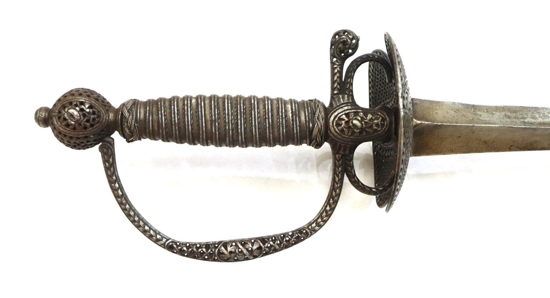 Close-up of an ornate silver-toned sword hilt and part of the blade on a white background.