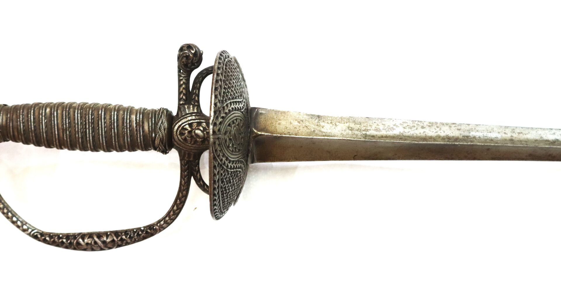 A close-up view of an antique sword with an ornate hilt and a slightly tarnished, straight blade, photographed on a white background.