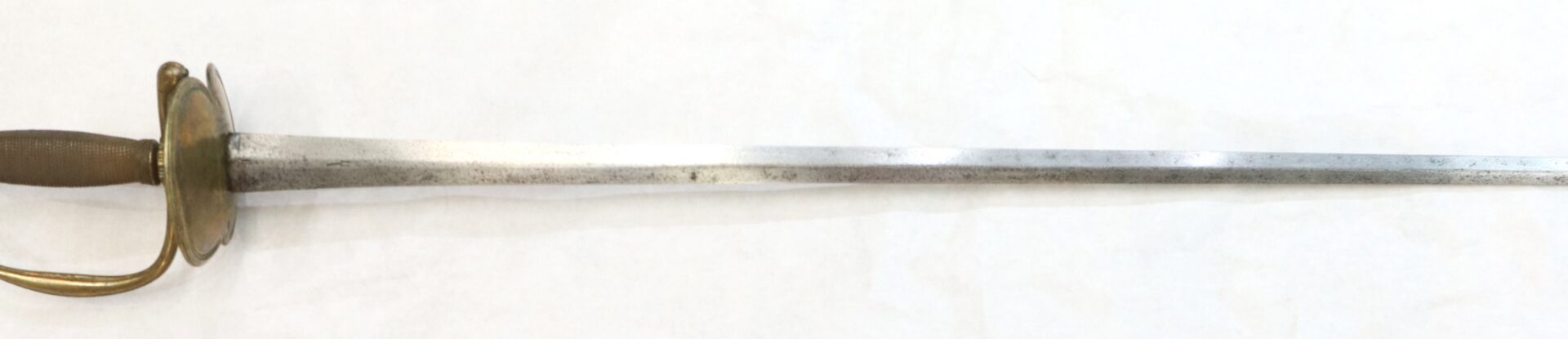 A fencing foil with a brass handguard, textured grip, and a long, narrow, slightly tarnished blade on a white background.