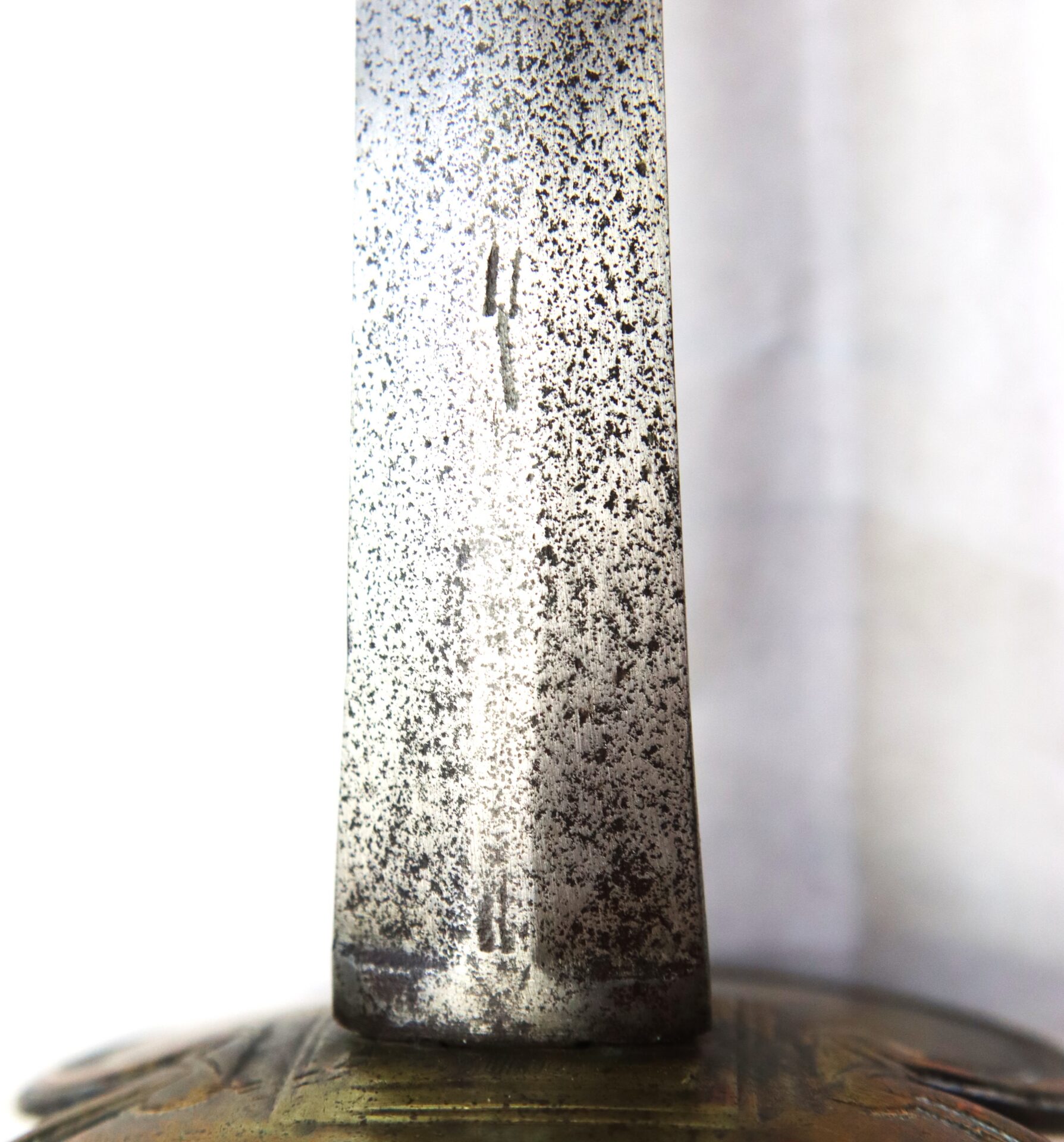 Close-up of a weathered sword blade showing signs of age and patina, with part of an ornate metal hilt visible at the bottom.