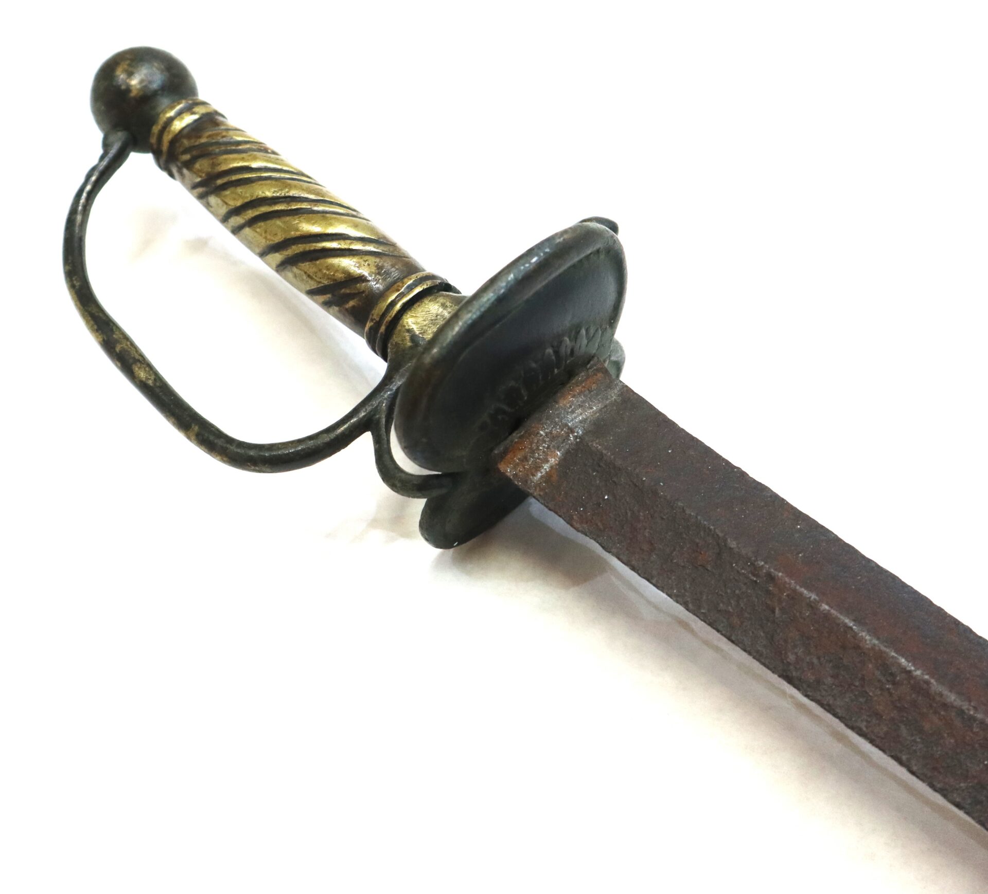 A close-up of an antique sword with a brass and black handle, a protective guard, and a rusty blade against a white background.