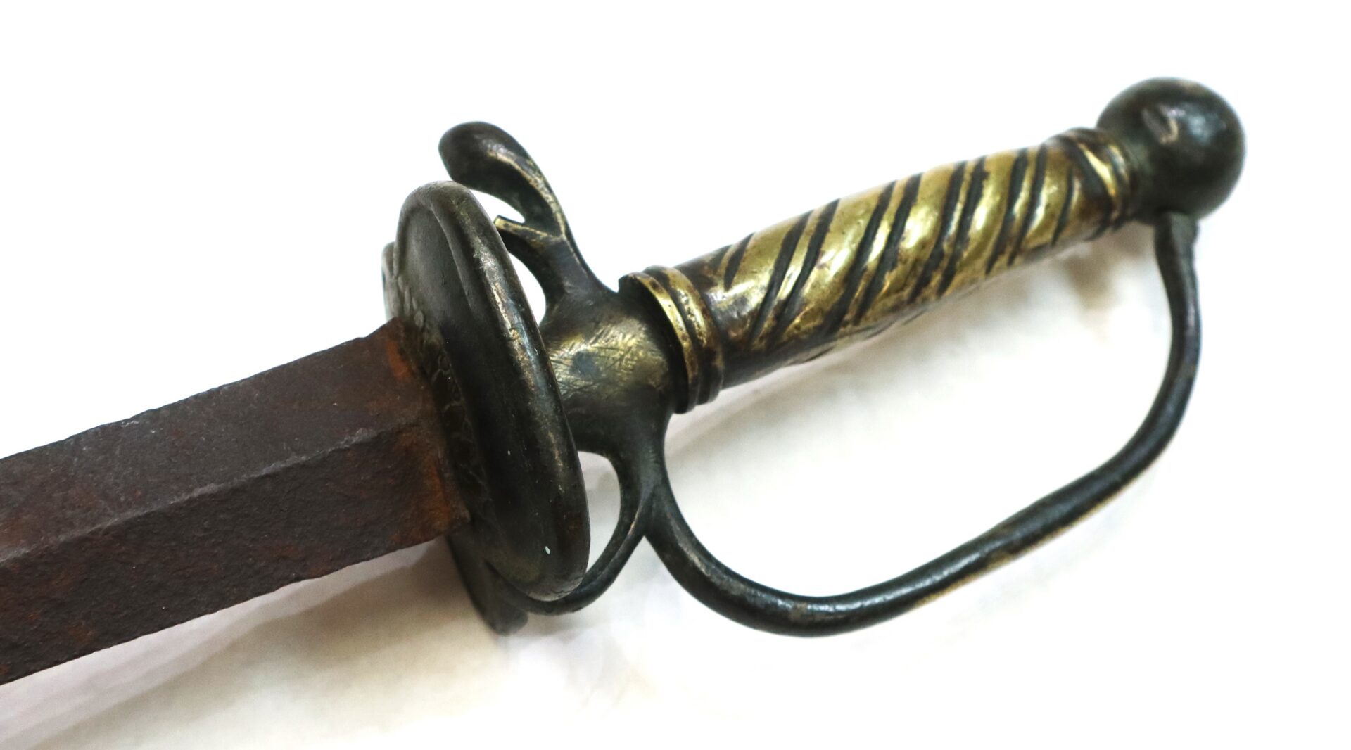 Close-up of an antique sword with a twisted metal handle, rounded guard, and a rusty blade on a white background.