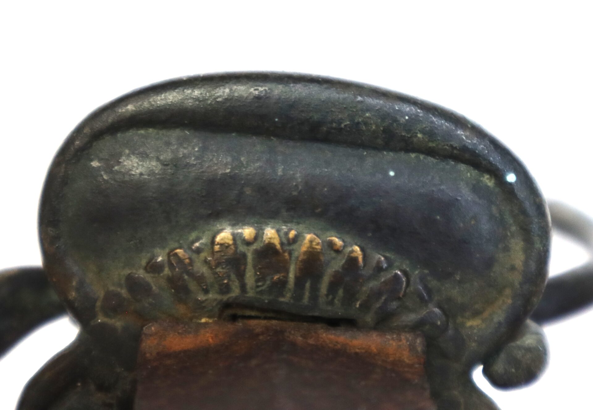 Close-up of an aged, tarnished metal object with engraved markings and a curved, rounded surface against a white background.