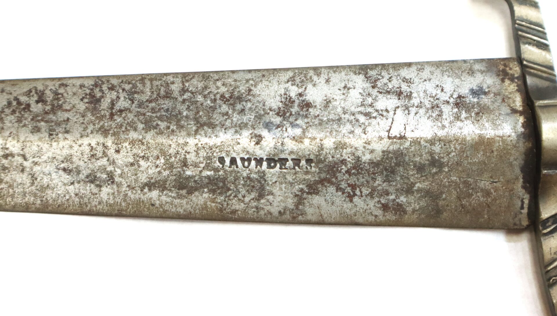 Close-up of a tarnished metal blade with the word "SAUNDER" engraved on its surface.