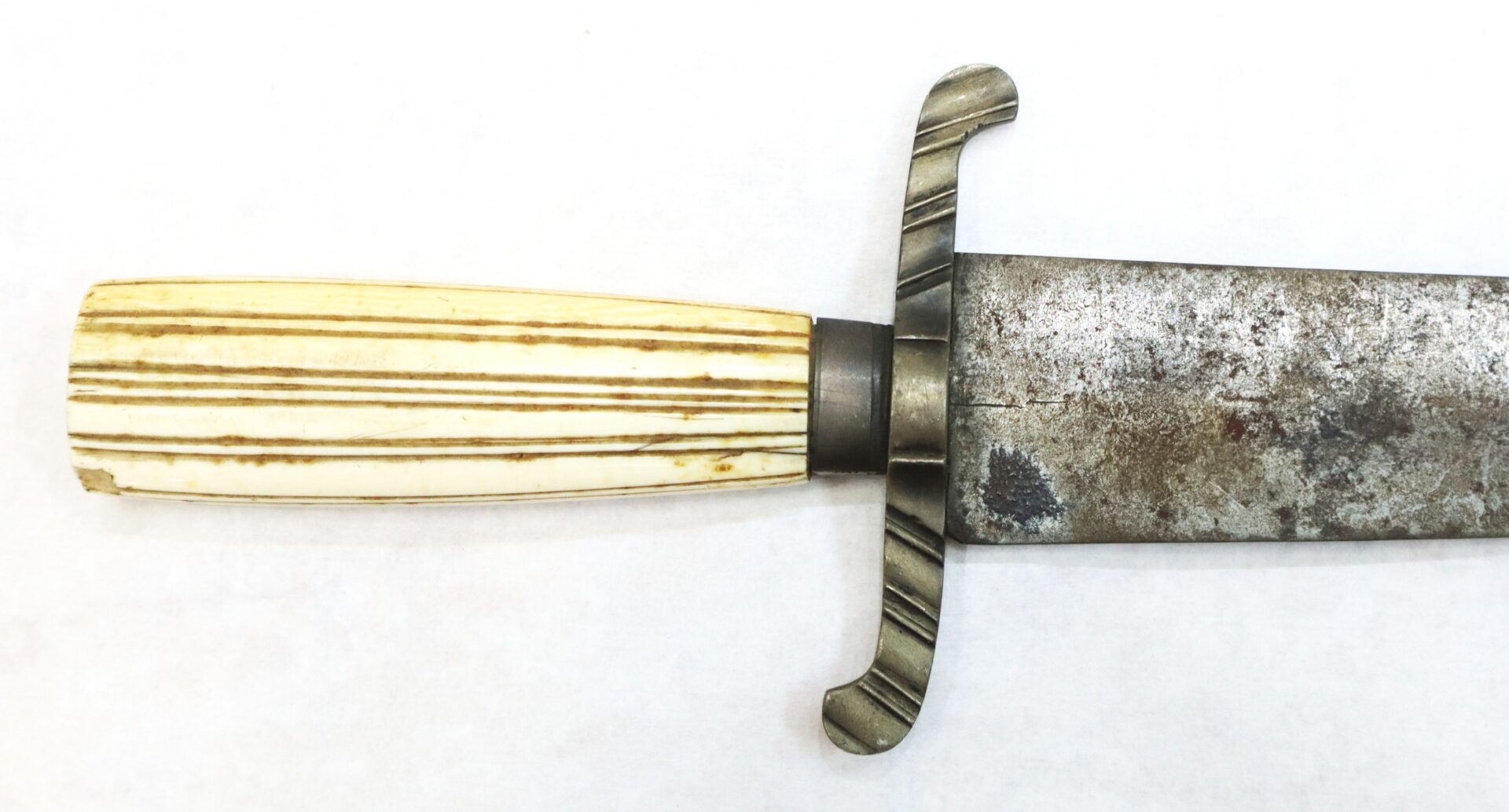 A close-up of a knife or short sword with a ribbed bone handle, metal crossguard, and a weathered steel blade on a white background.