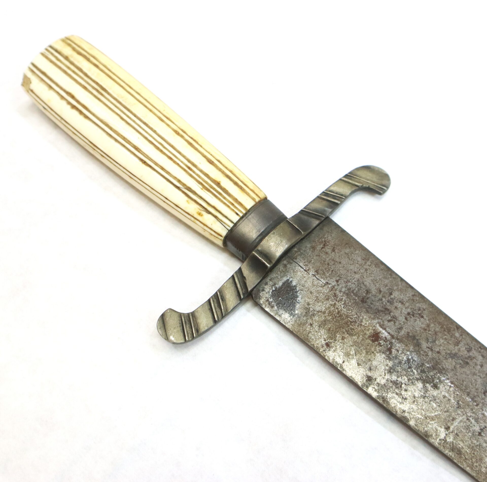 A close-up of a vintage knife with a metal guard, a stained and weathered blade, and a light-colored, striped handle.
