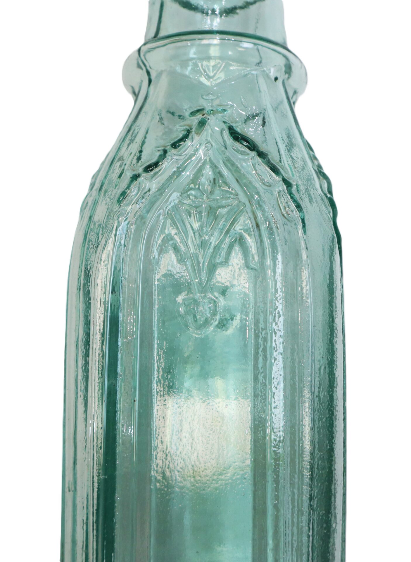 Close-up view of a vintage green glass bottle with embossed decorative patterns on its surface.