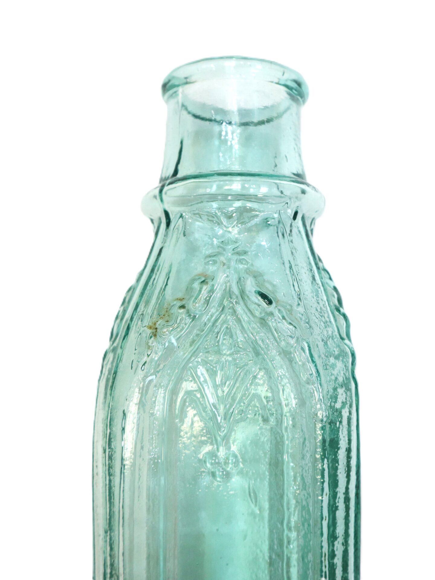 Close-up of the neck and top of a vintage, clear blue-green glass bottle with ornate embossed patterns.