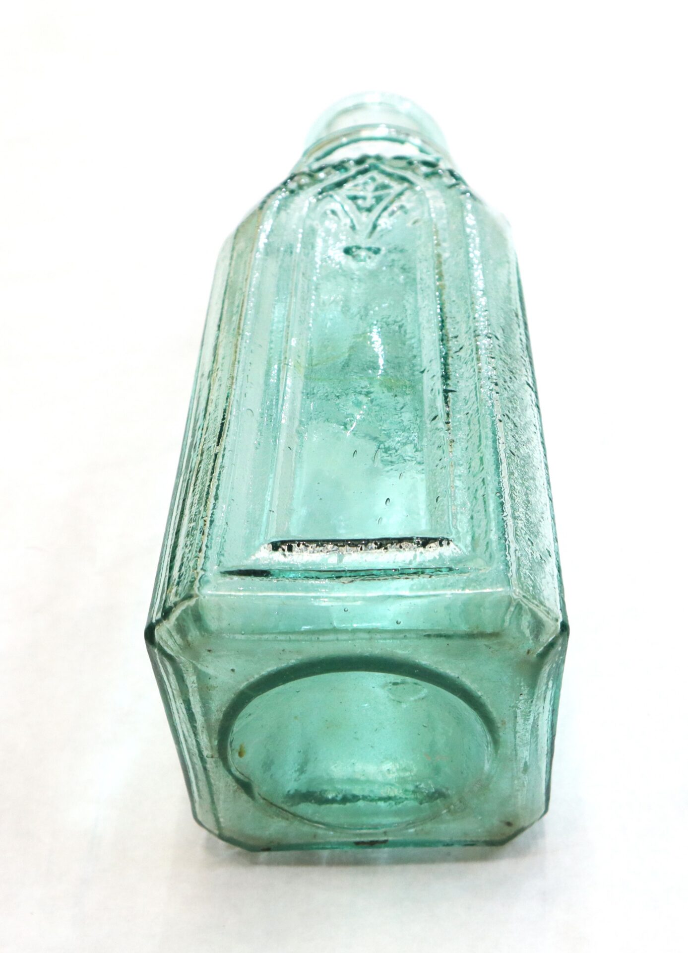 Clear greenish vintage glass bottle with a hexagonal base, lying on its side against a white background.