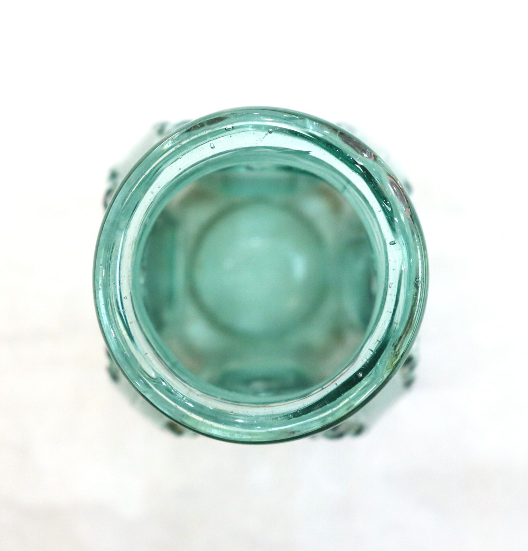A top-down view of an empty, transparent teal glass bottle with a wide opening, set against a plain white background.