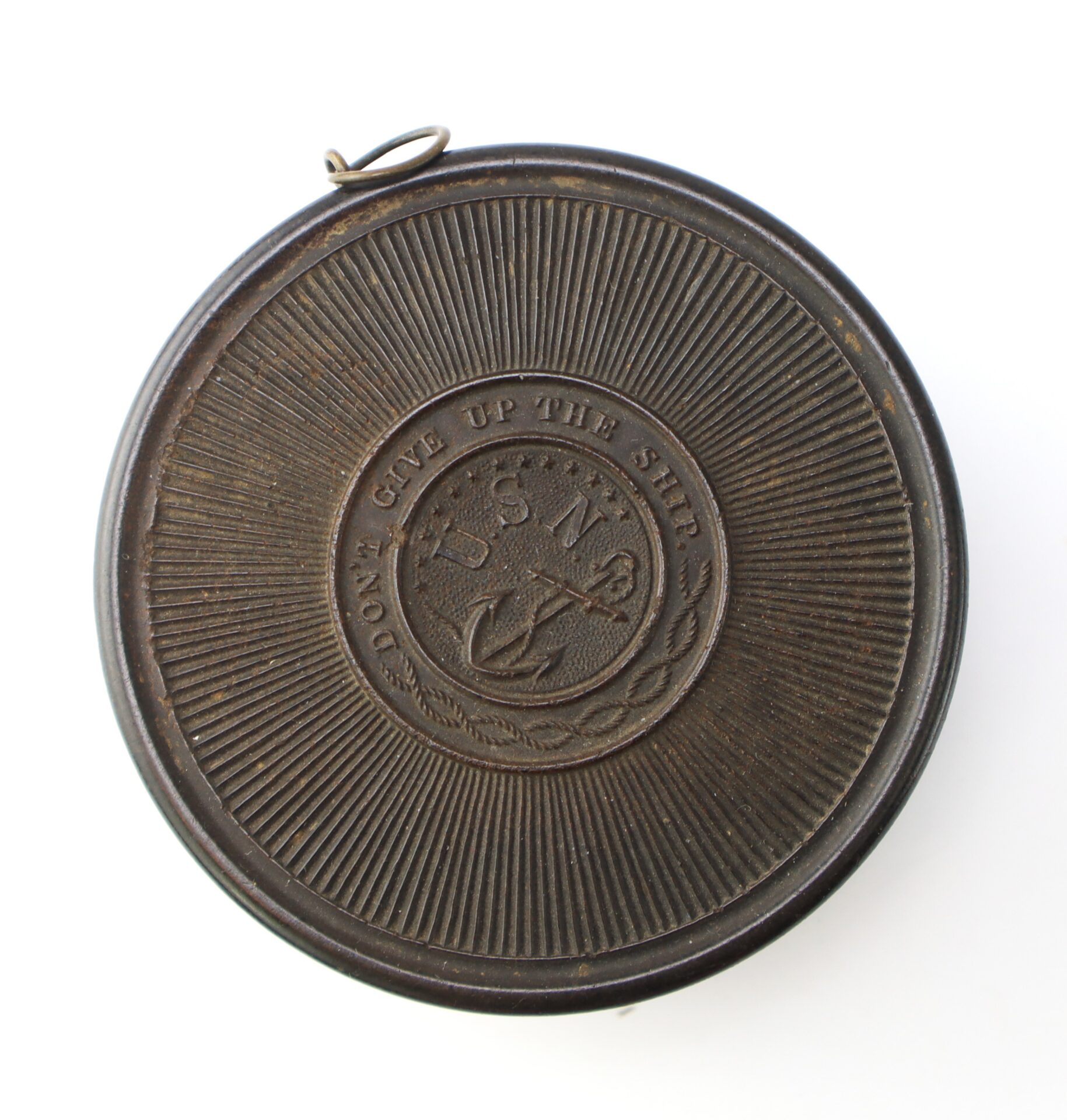 Round, dark metal box with a raised emblem featuring an anchor and the letters "U.S.N." surrounded by the words "Don't Give Up The Ship.