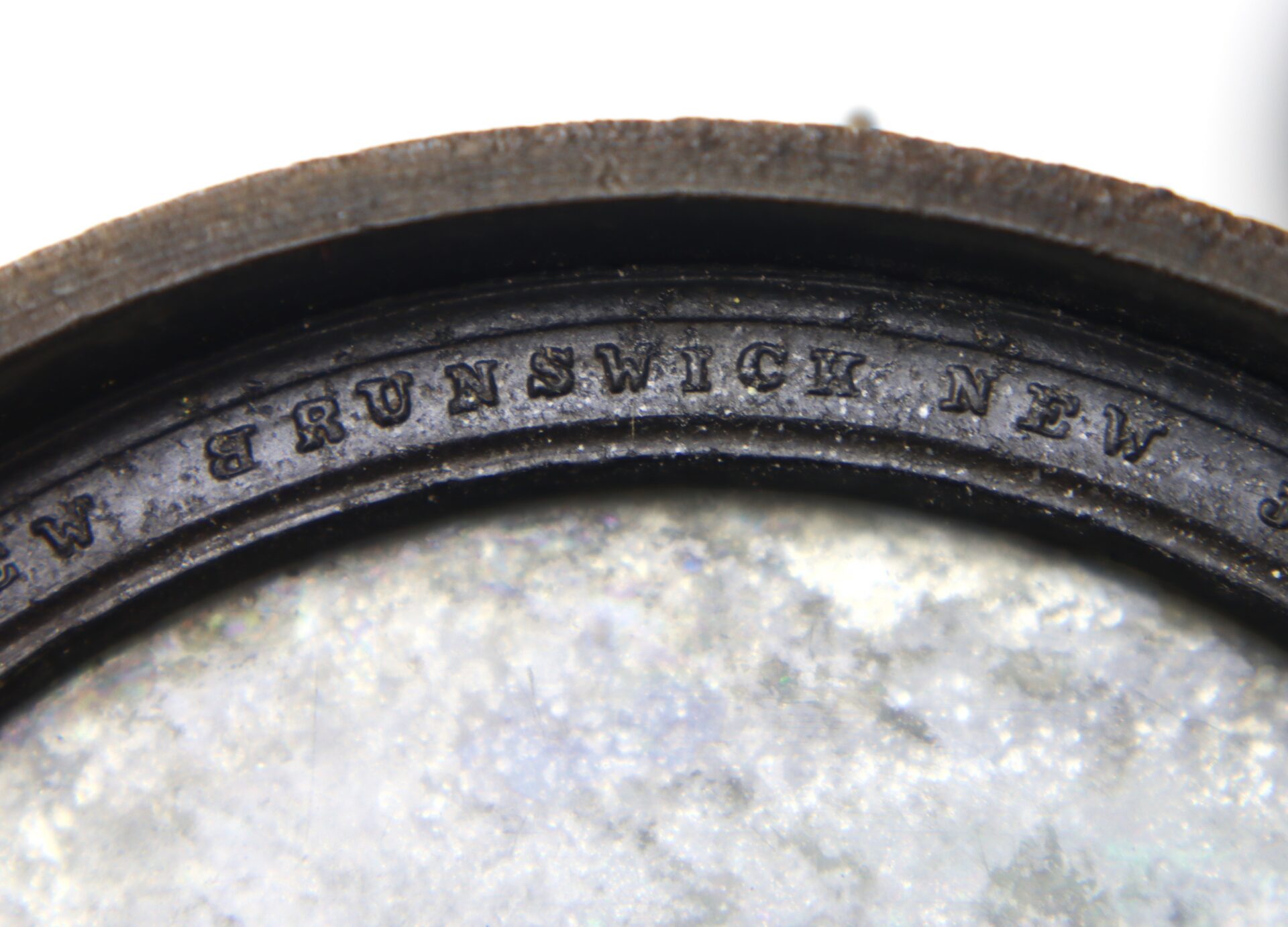 Close-up of an old metallic object with the inscription "BRUNSWICK NEW JER" visible along the curved edge.
