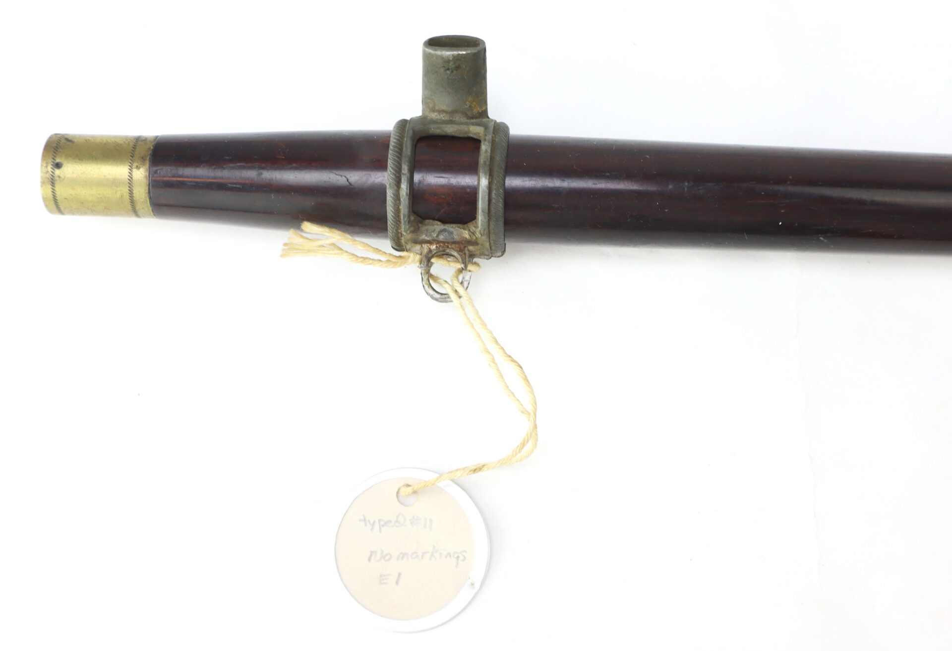 A close-up of a Civil War–Era Fife with Brass Fittings, Gettysburg Provenance, showing its brass tip and metal fitting, attached to a string with a round white “Type #11 No markings E1” tag.
