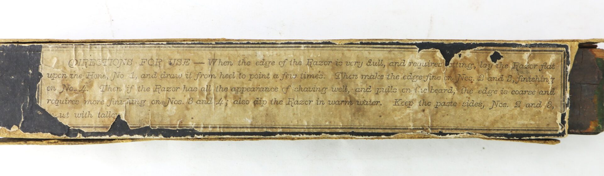 A worn rectangular label on a box of the J.R. Torrey’s Patent Razor Strop, 1861, displays faded instructions for use, with visible damage along the edges of both the label and box.