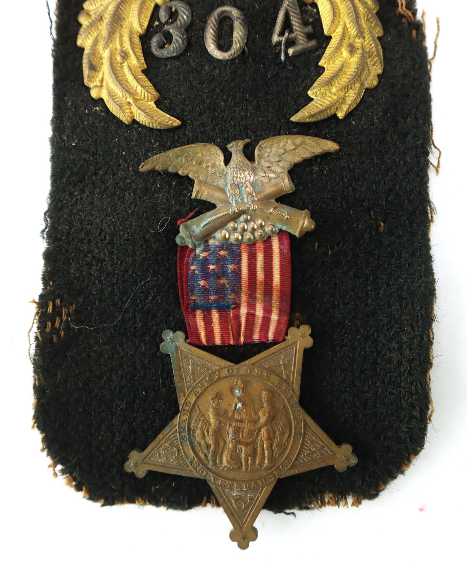 A vintage military medal featuring an eagle, a U.S. flag ribbon, and a bronze star-shaped medallion with embossed figures, mounted on black fabric with a "304" insignia above.