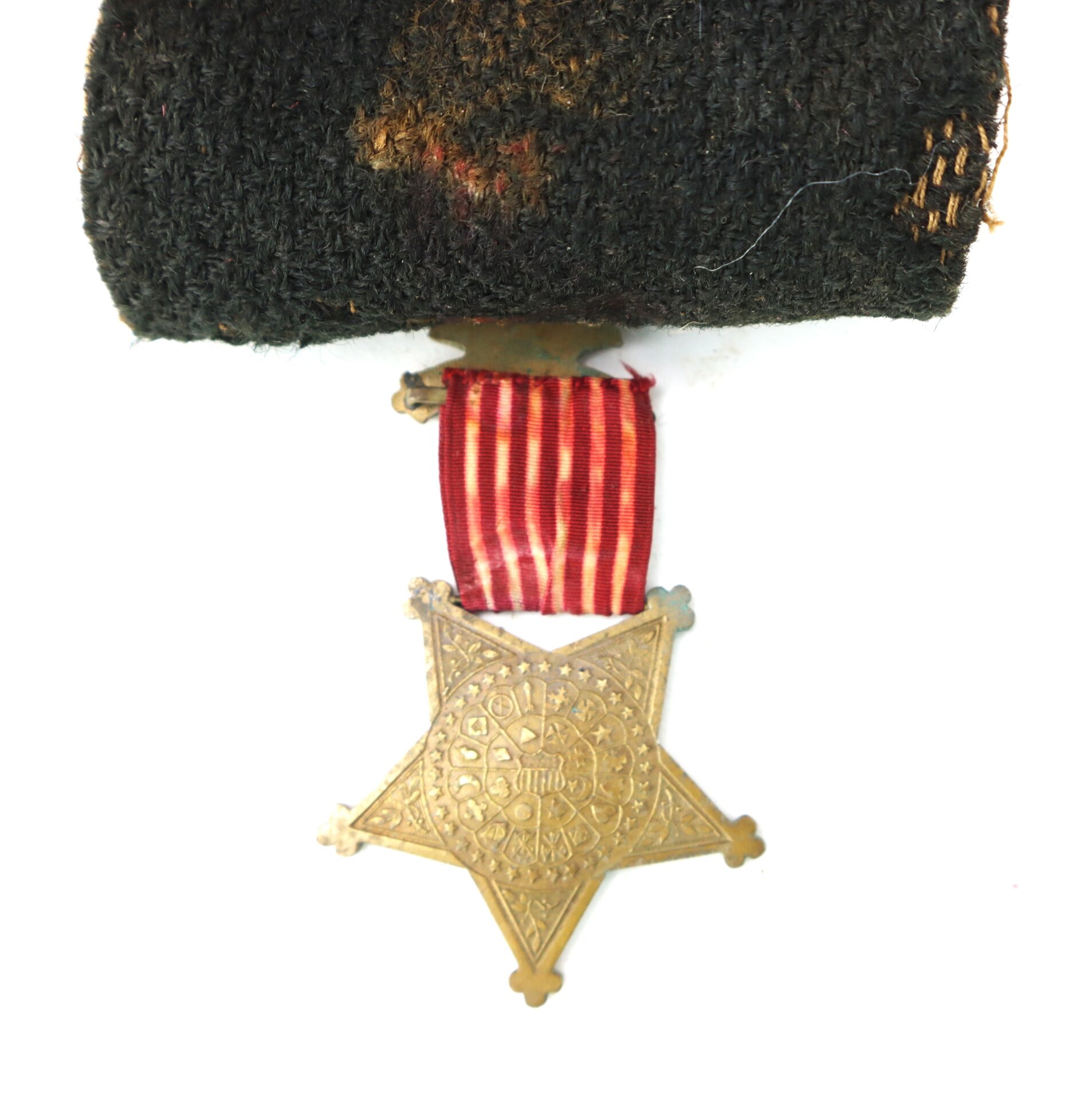 A gold star-shaped medal with ornate detailing hangs from a red and white striped ribbon attached to a piece of black fabric.