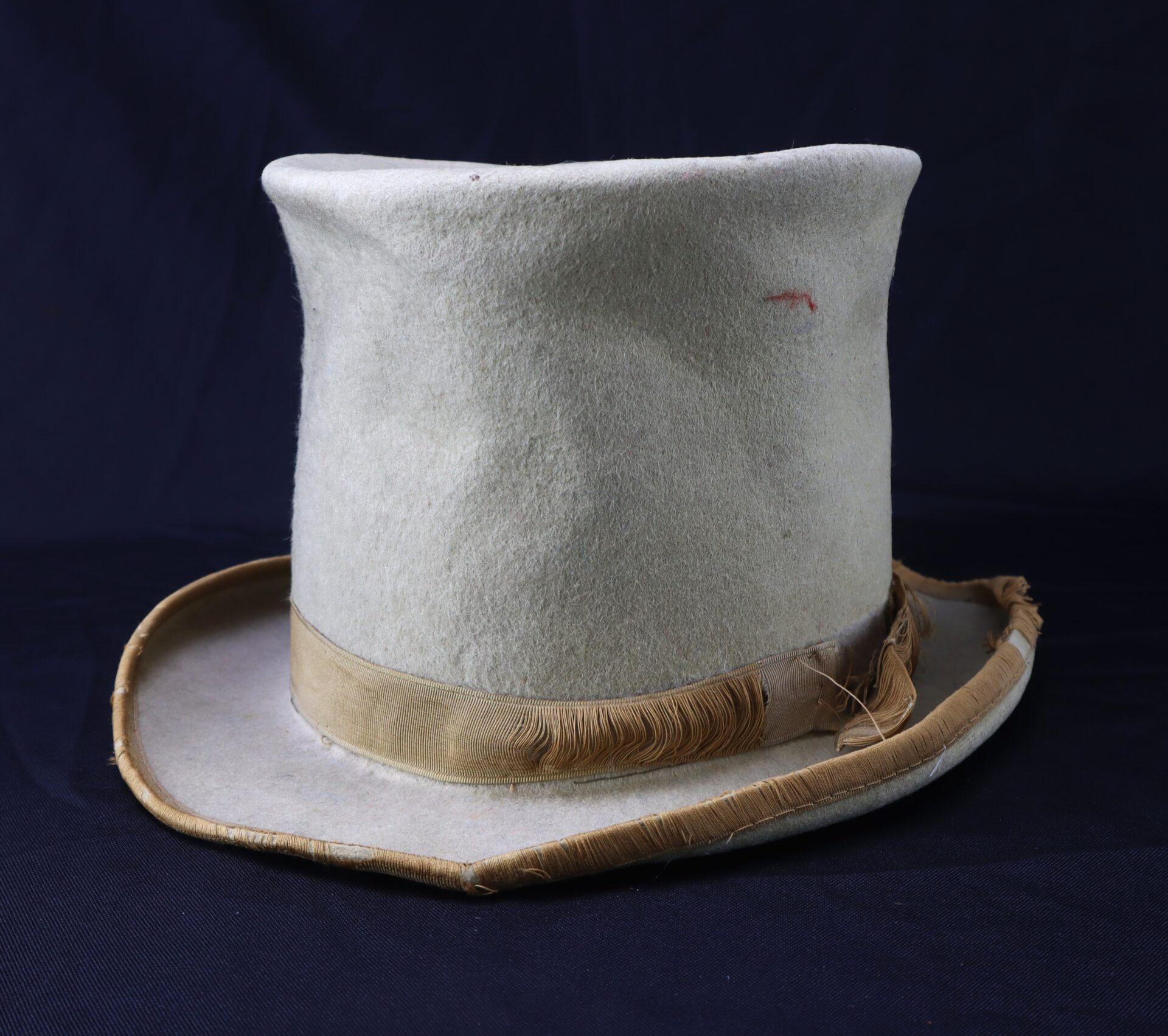 The Awesome Top Hat for the 1888 Republican Campaign features a worn look, light color, damaged brim, and frayed ribbon, displayed against a dark background.