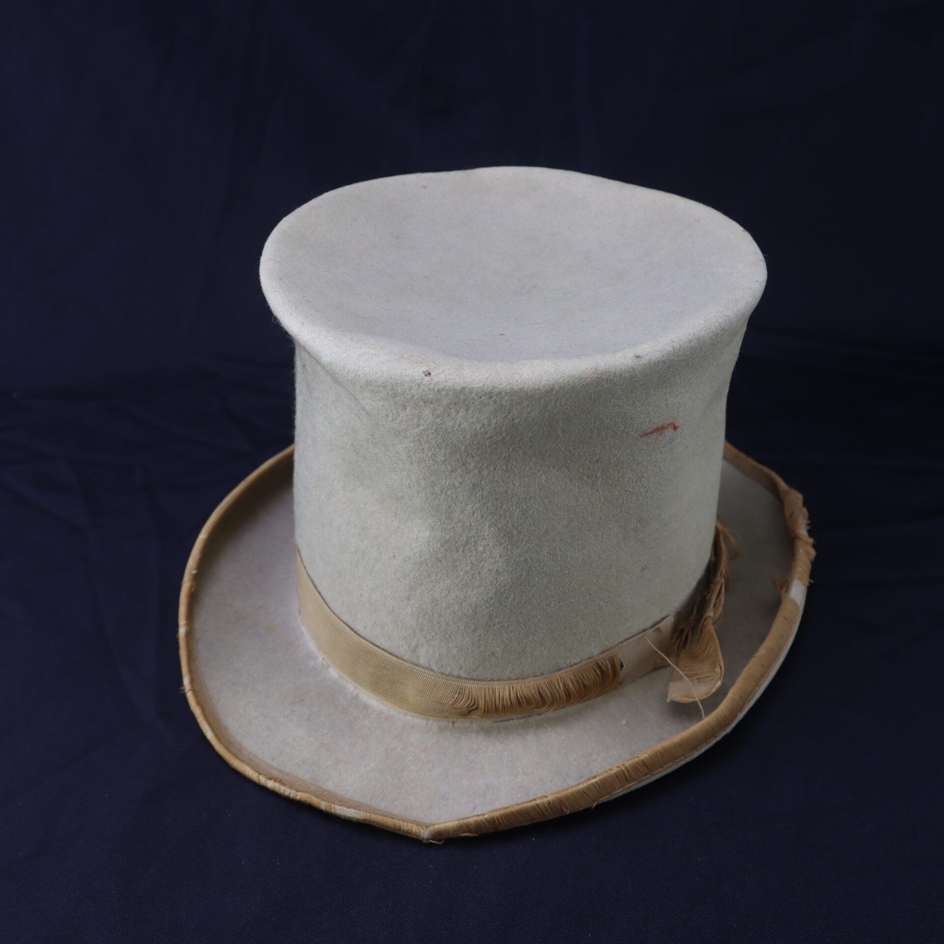 An Awesome Top Hat for the 1888 Republican Campaign, featuring a light color, tall crown, wide brim, gold band, and visible signs of wear, set against a dark background.