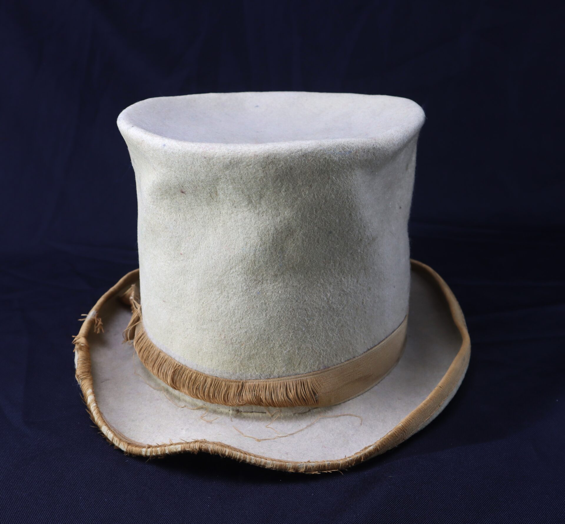 The Awesome Top Hat for the 1888 Republican Campaign features a worn white crown, beige ribbon, and fraying brim, shown against a dark background.