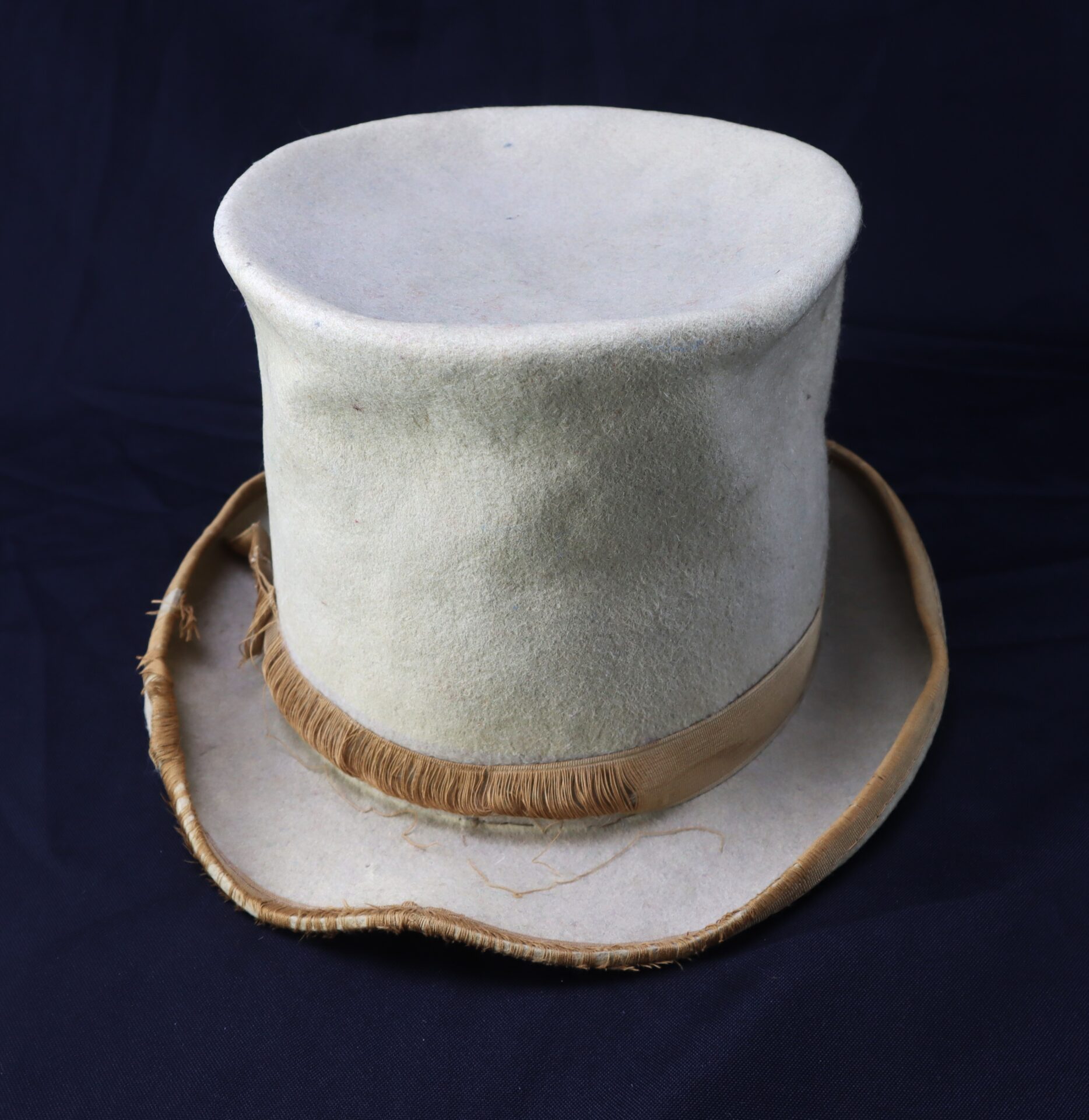 The Awesome Top Hat for the 1888 Republican Campaign, featuring a worn white finish, wide brim, and beige ribbon, rests on a dark surface.