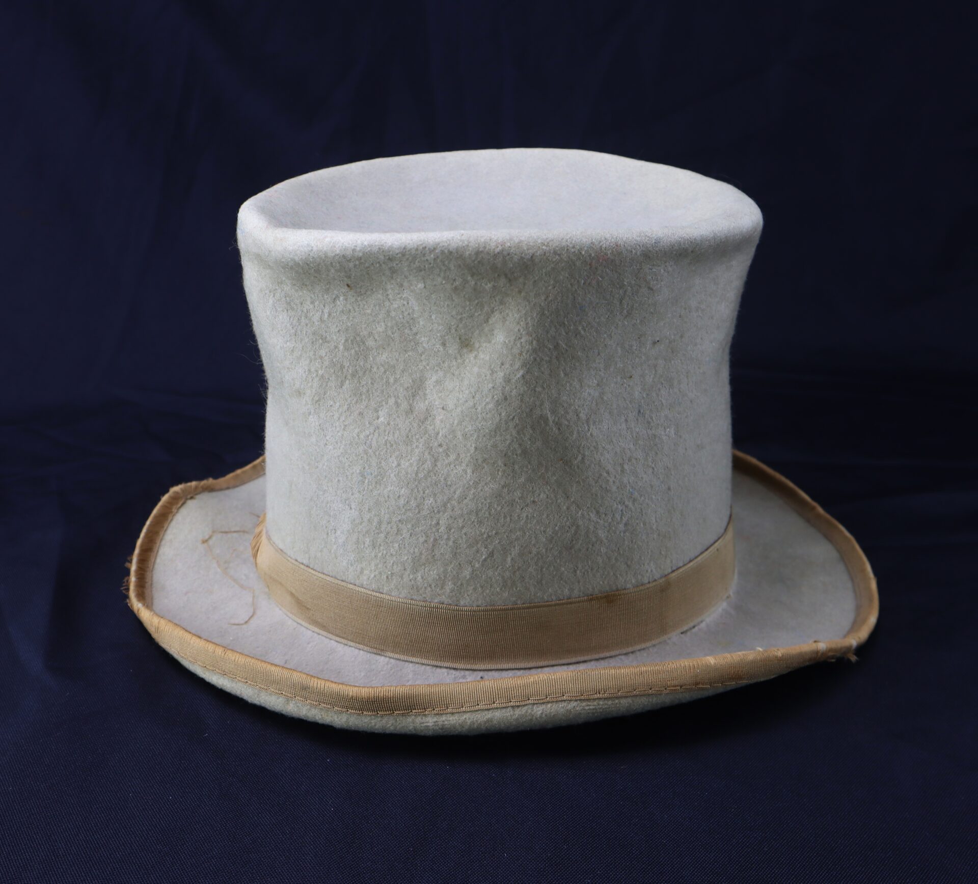 The Awesome Top Hat for the 1888 Republican Campaign is a light gray, slightly worn top hat with a beige ribbon band, shown against a dark background.