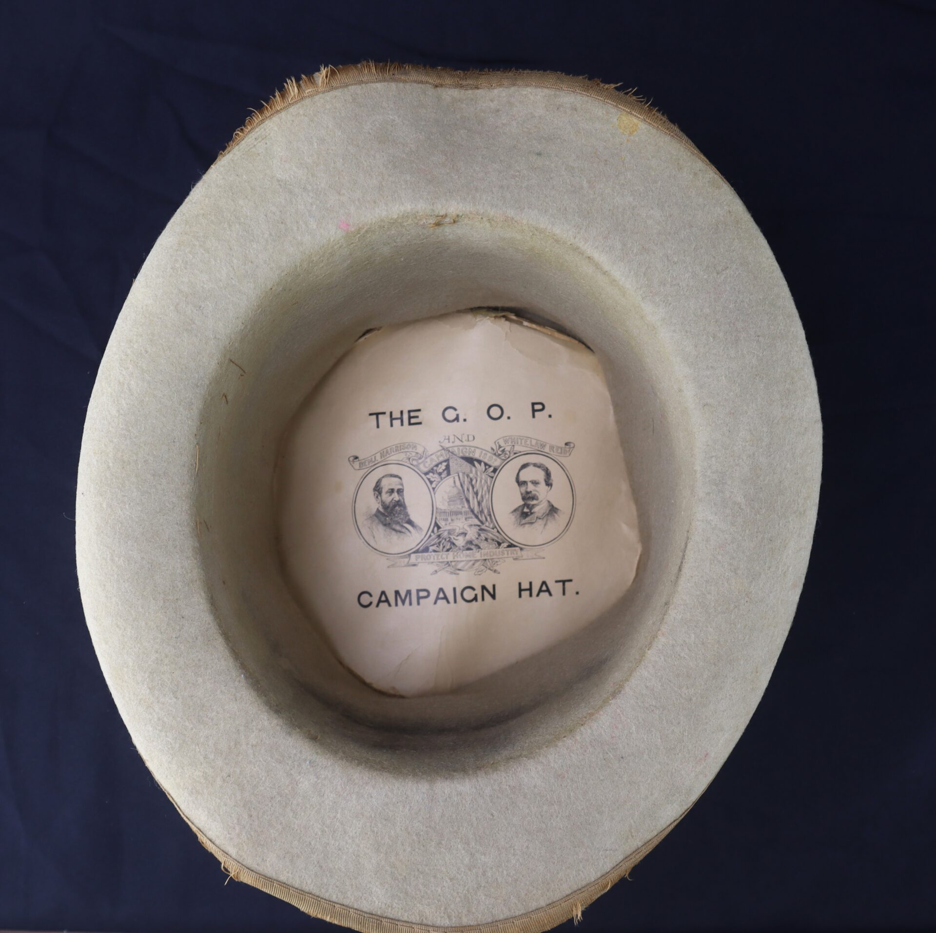 Top-down view of the Awesome Top Hat for the 1888 Republican Campaign, featuring its interior paper label with portraits, decorative details, and “THE G.O.P. CAMPAIGN HAT” text.