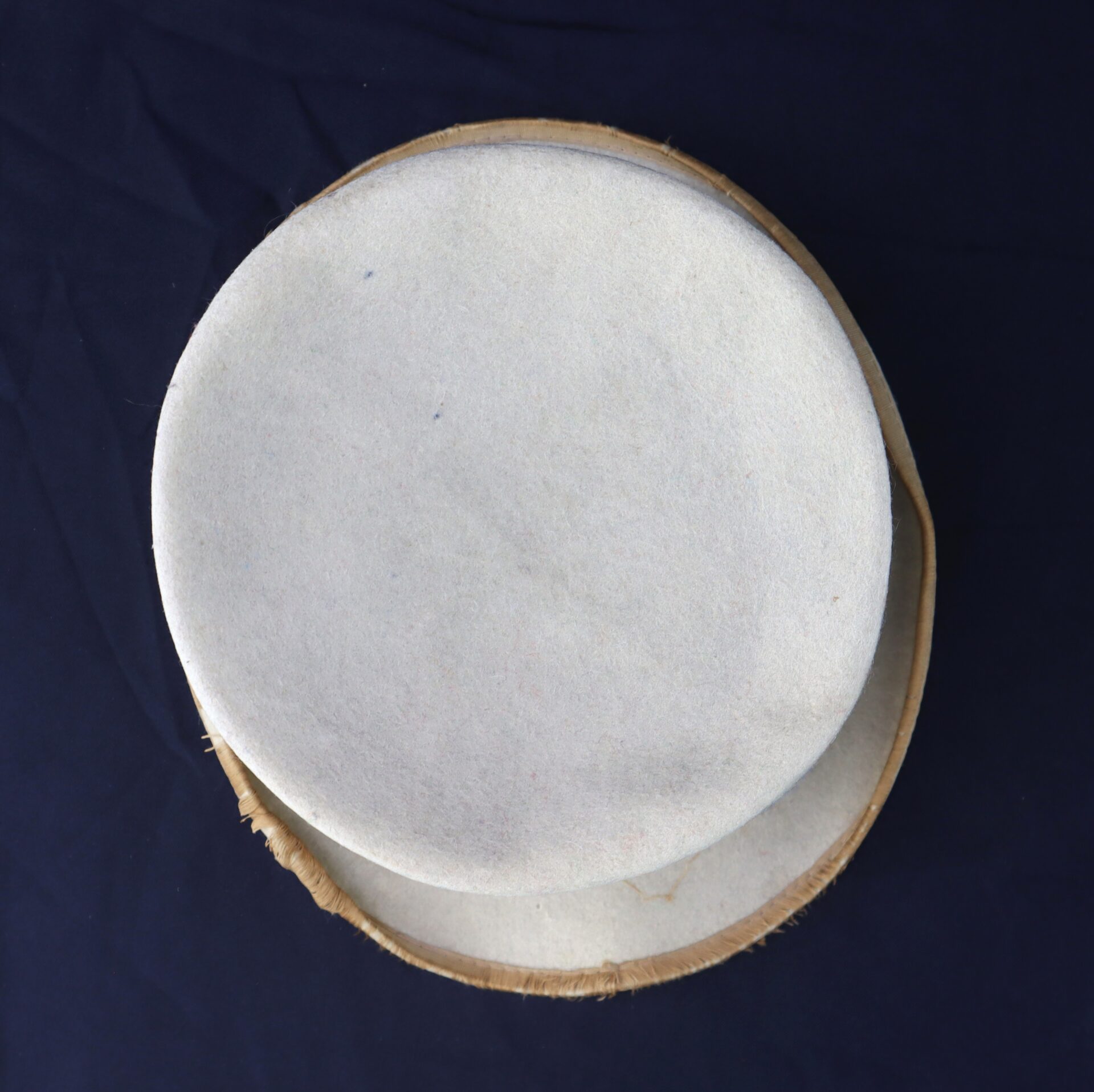 Two round, white felt pieces are stacked on a circular, unfinished brown base, forming the Awesome Top Hat for the 1888 Republican Campaign, displayed on a dark surface.