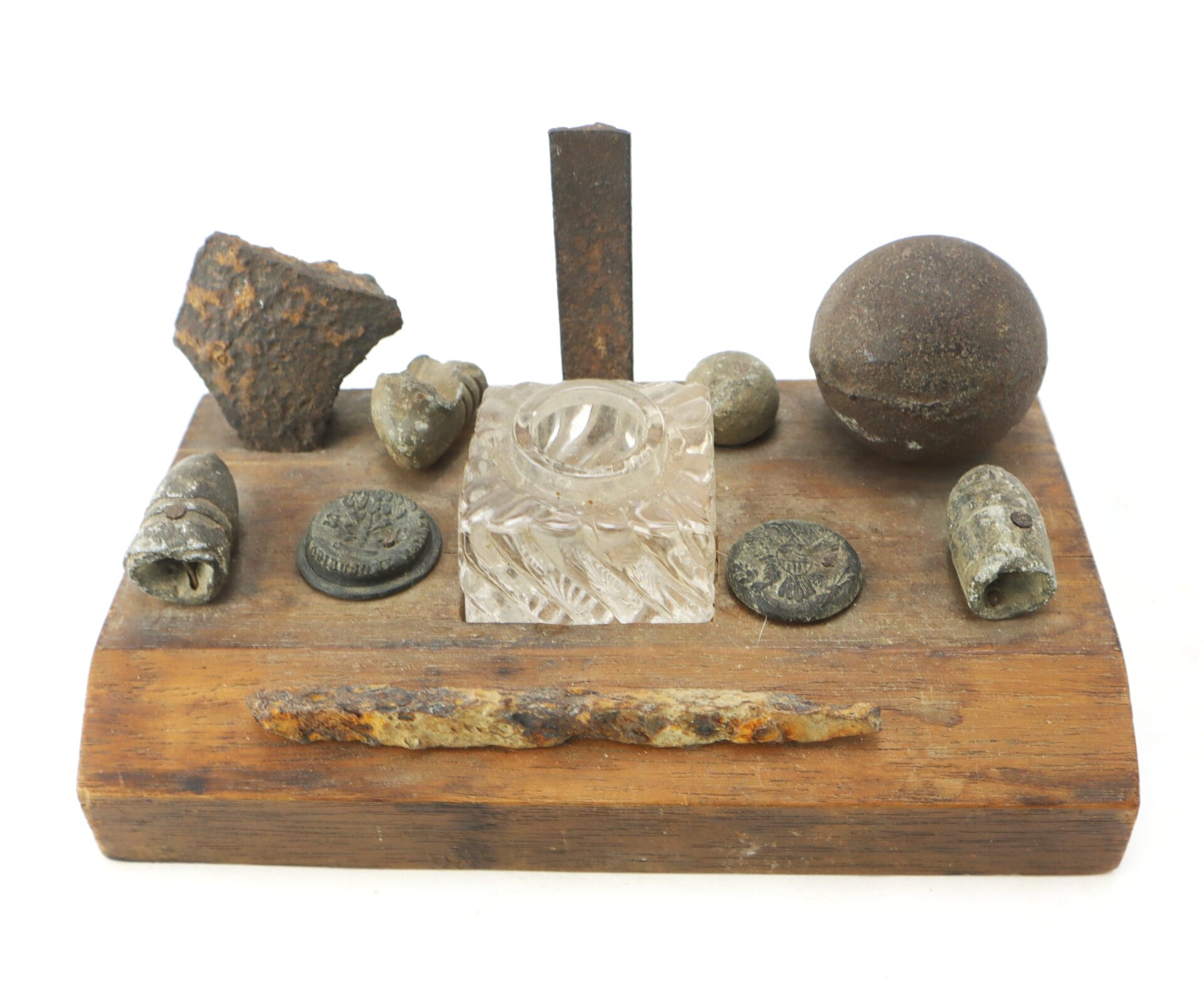 A wooden display holds various old metal artifacts, a glass inkwell, a rusted bar, and a spherical object, all arranged in an orderly manner.