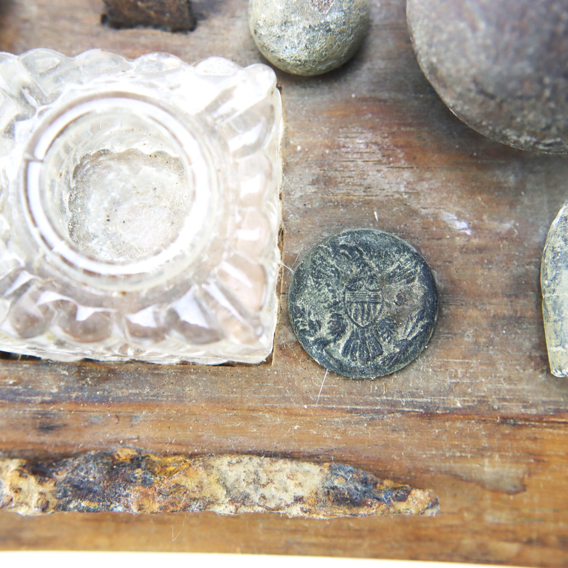 A close-up of a decorative glass inkwell and an old metal button with an eagle emblem on a wooden surface.