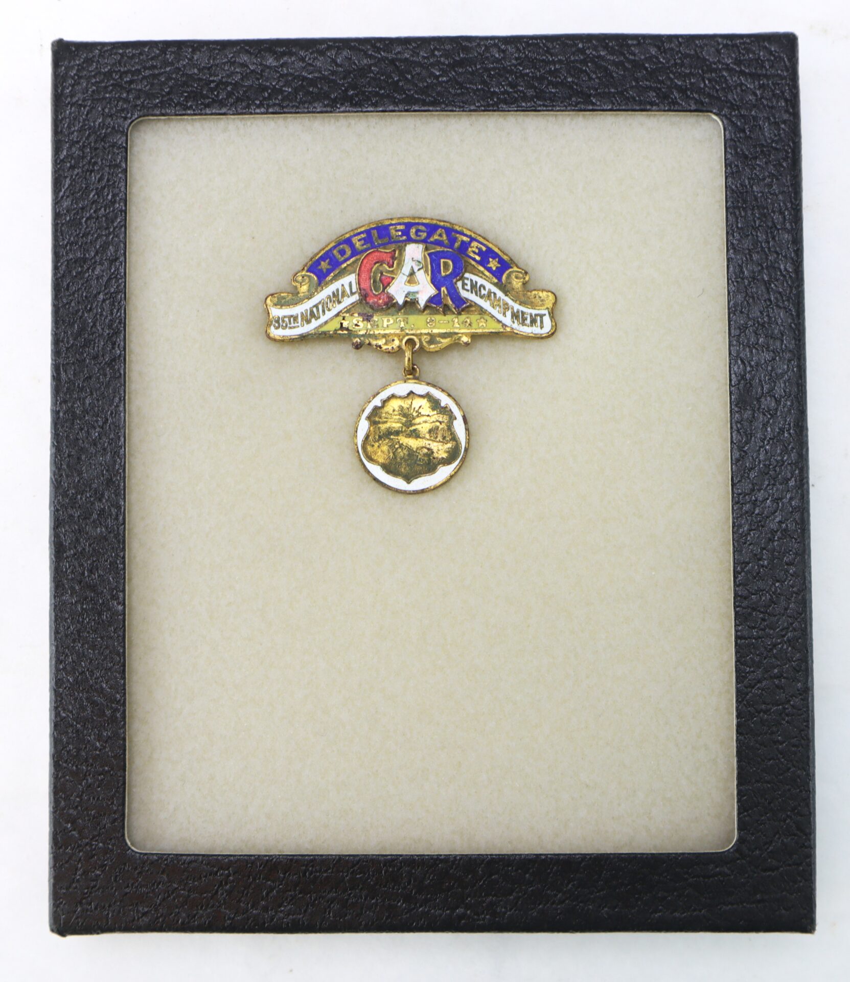 A delegate badge with a ribbon reading "GAR National Encampment" and a gold medallion, displayed in a black-frame case.