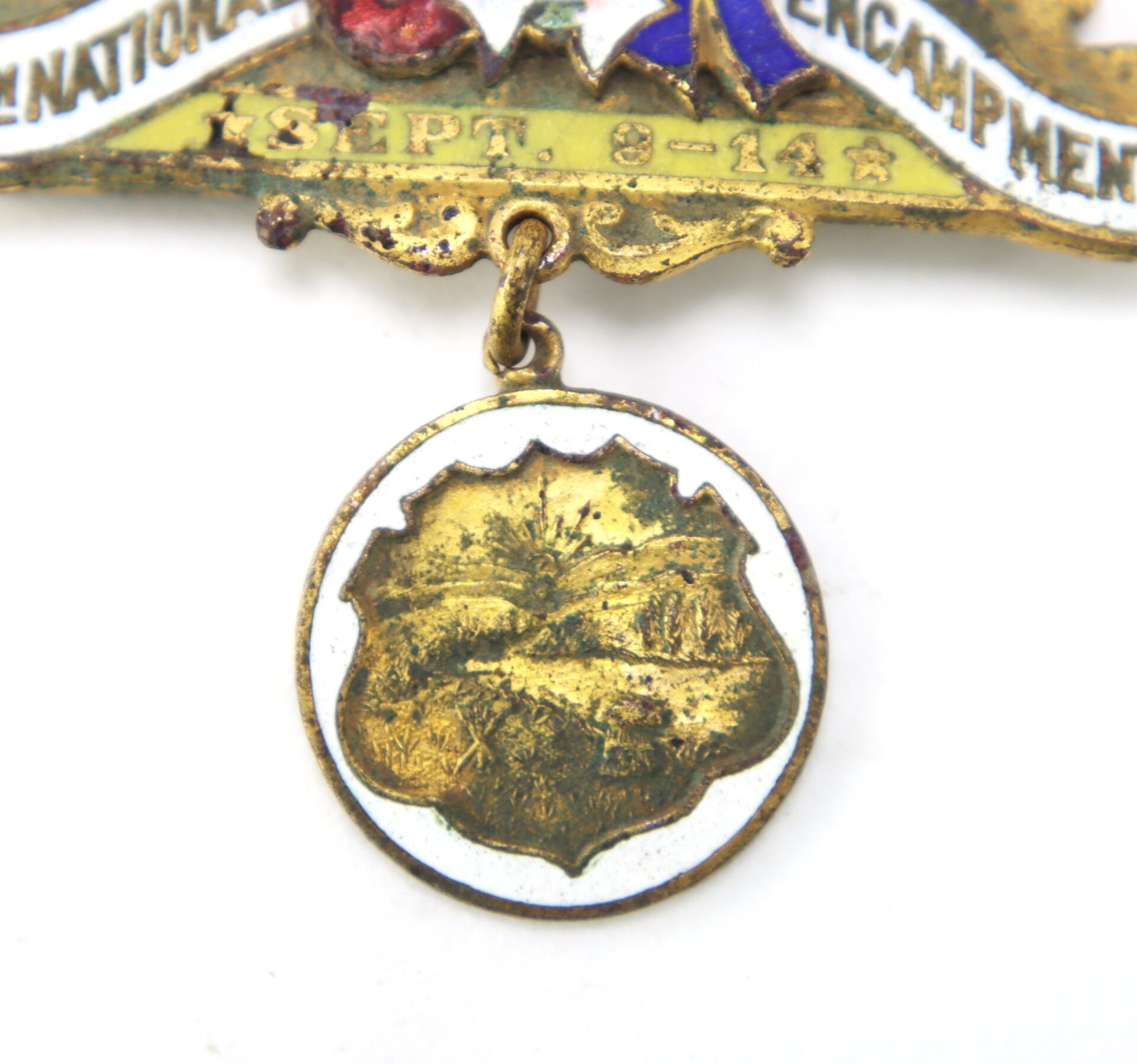 Close-up of a vintage medal with a round, tarnished gold pendant featuring a landscape scene, attached to an enamel pin with partially visible text and dates "SEPT. 8-14".