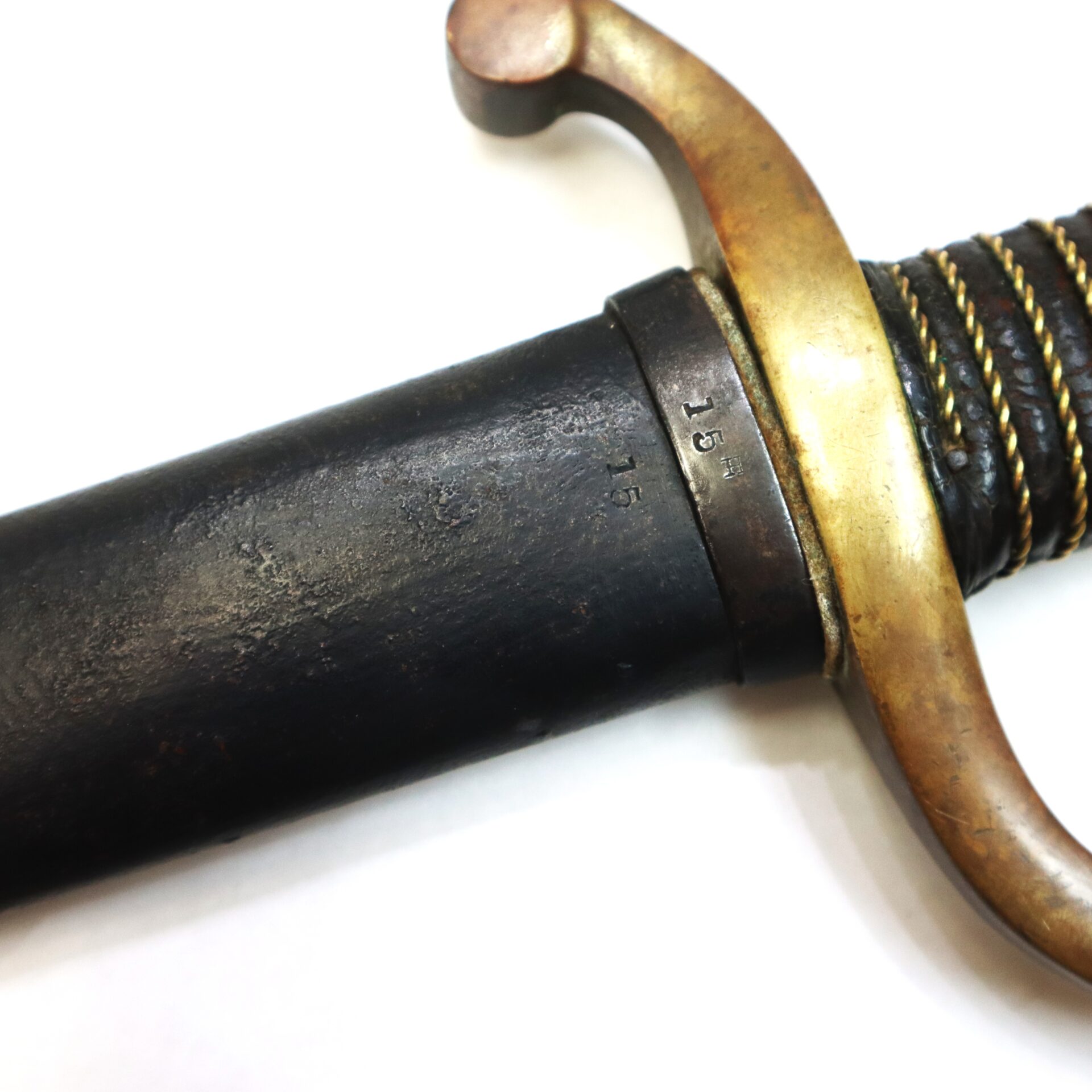 Close-up of a sword with a brass guard, black scabbard, and visible number "15" engraved on the metal near the hilt.