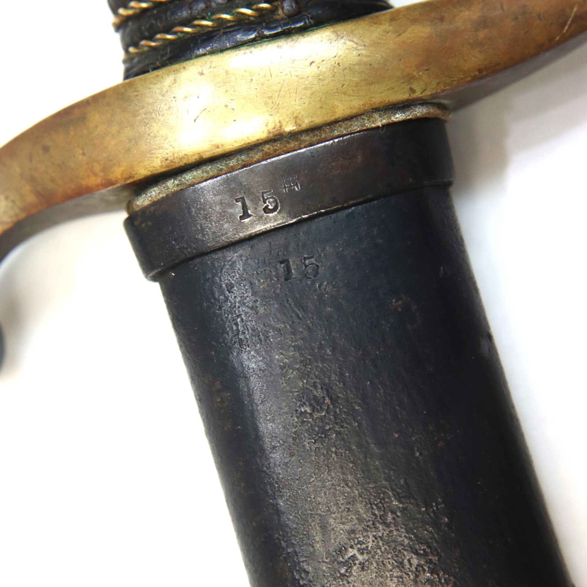 Close-up of a sword hilt featuring a brass guard and metal grip with the number "15" stamped twice on the metal surface.