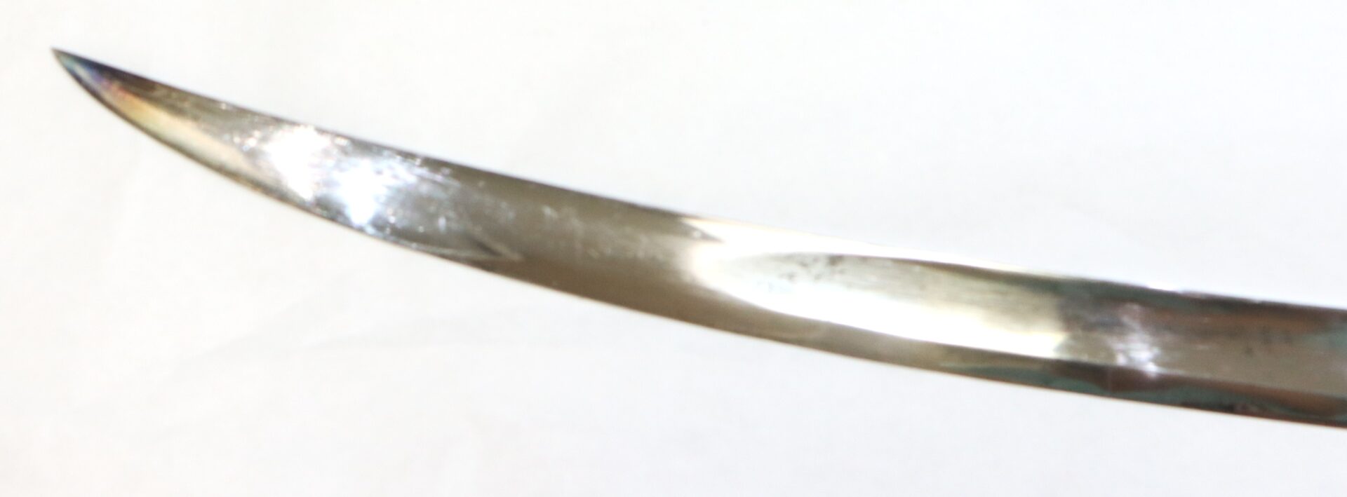 Close-up view of the curved, pointed tip of a polished metal blade against a plain white background.