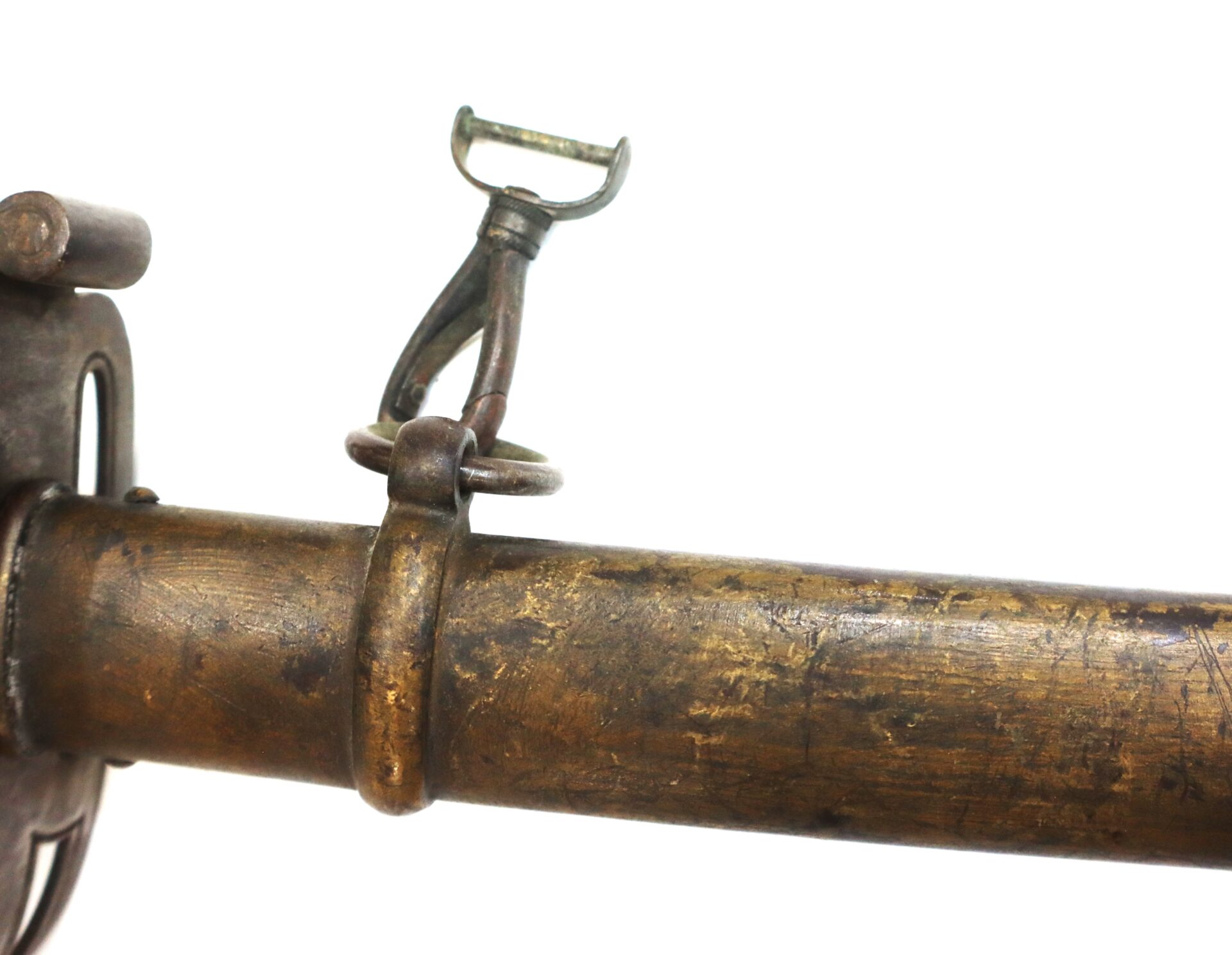 Close-up of a worn, brass-colored metal tube with a swivel and clamp attachment, likely part of an antique firearm or cannon, set against a white background.