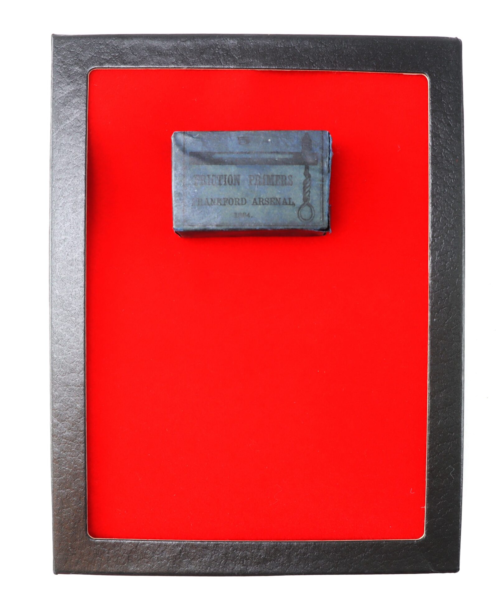 A small, rectangular antique box labeled "Section Primers Hartford Arsenal 1864" is displayed on a bright red background in a black frame.