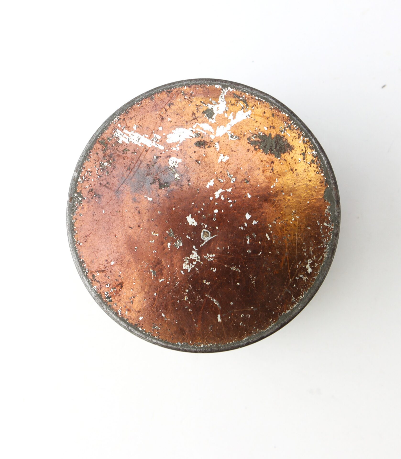 A round, worn copper object with scratches and tarnish, viewed from above against a plain white background.
