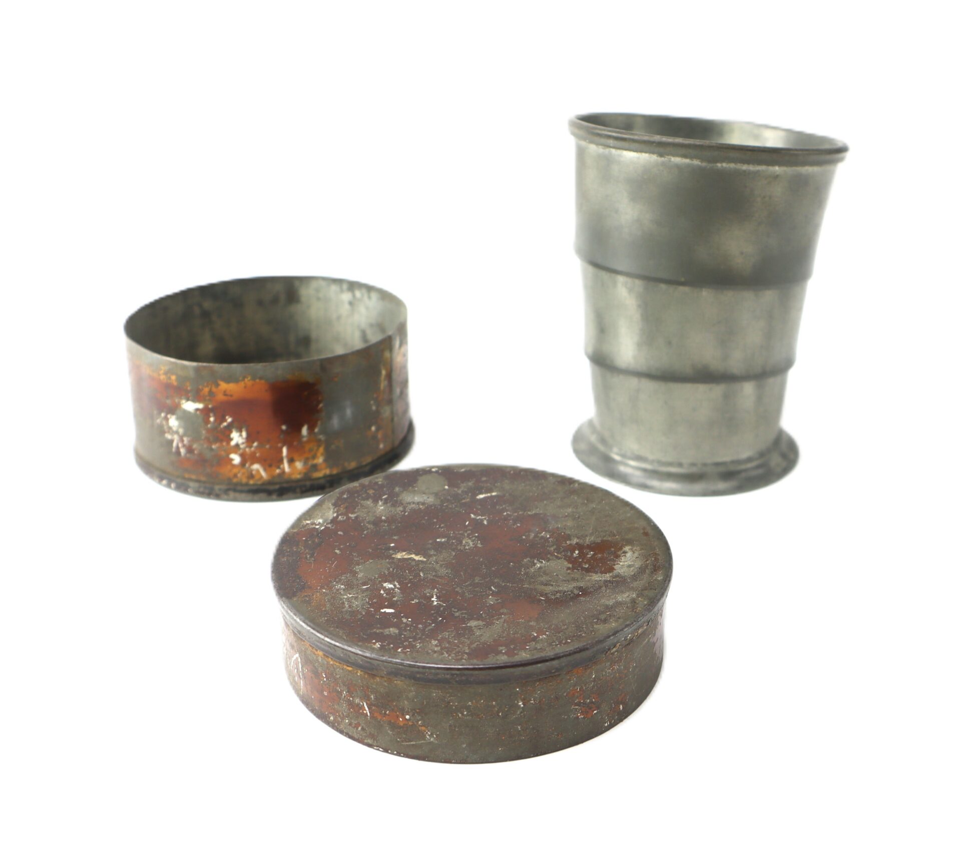 Three vintage metal containers: one cylindrical cup, one open round tin, and one closed round tin, all showing signs of rust and wear.