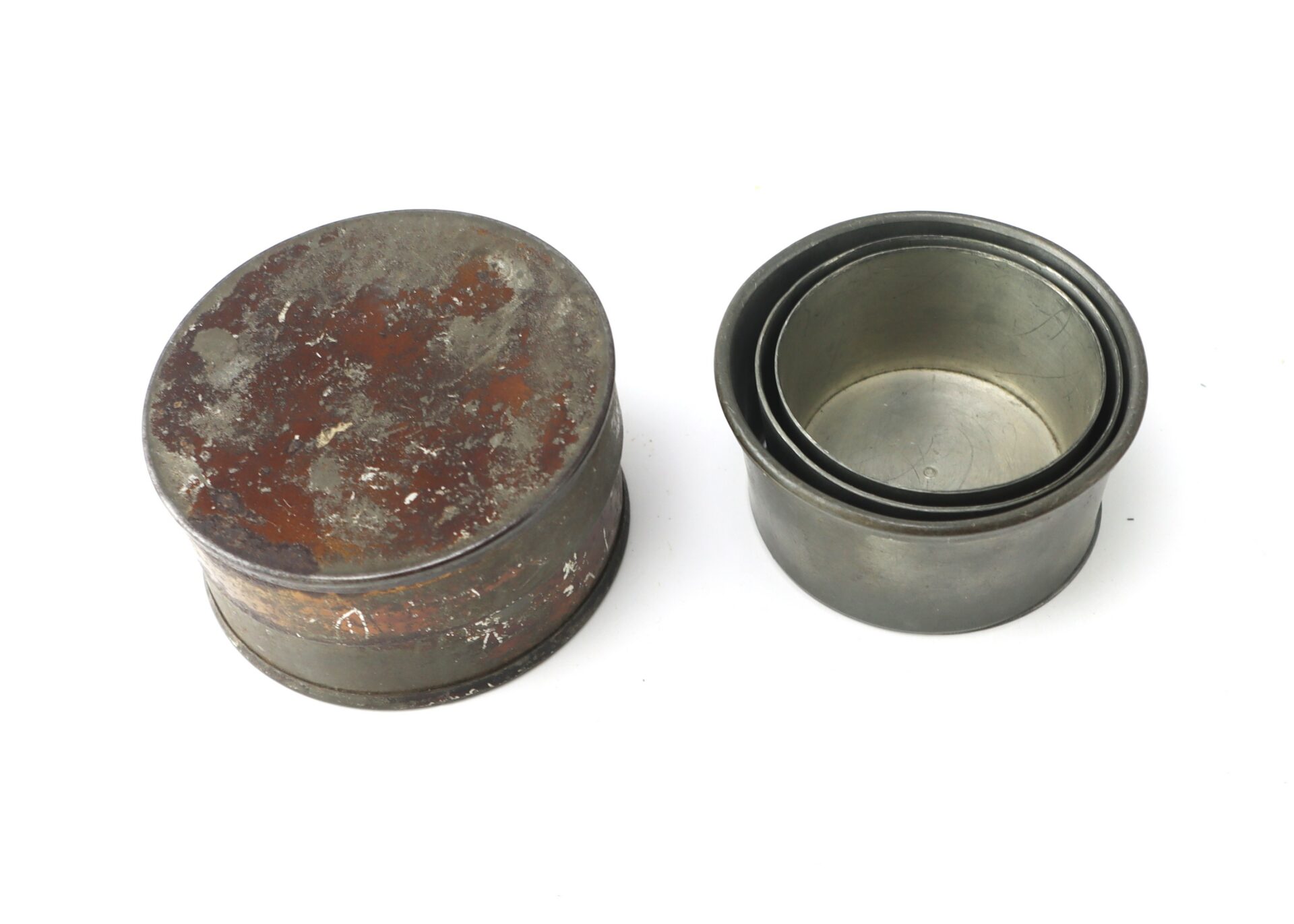 Two metal biscuit cutters are shown, one with a rusted lid on and the other open, revealing multiple nested circular cutters inside.